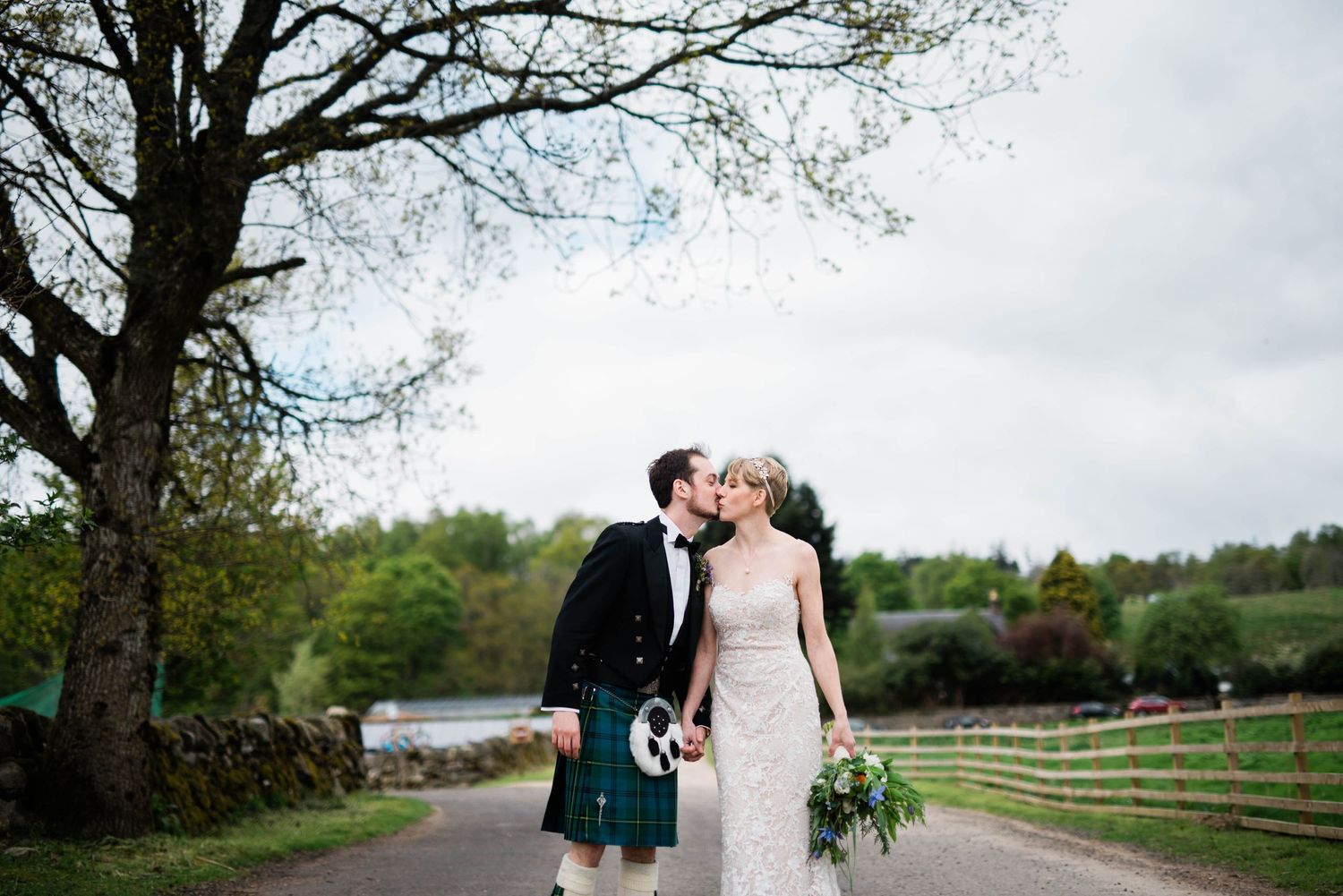 A couple poses on a country road with rustic fencing and rolling hills in the background.