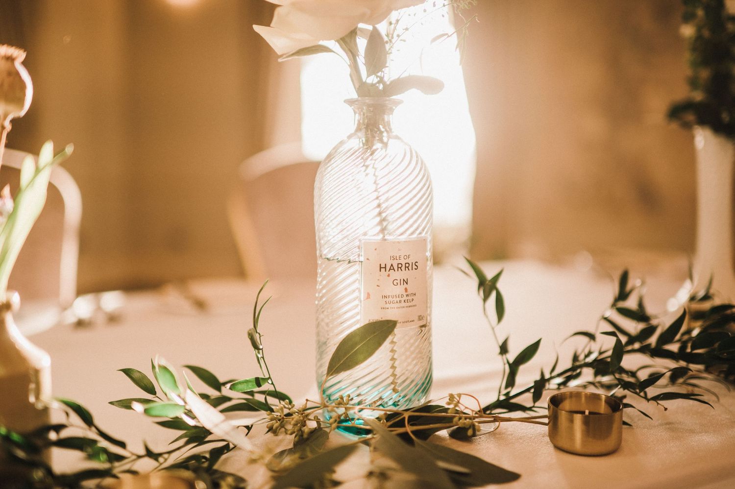 Wedding table setting with decorative white bottle, greenery, and soft ambient lighting.