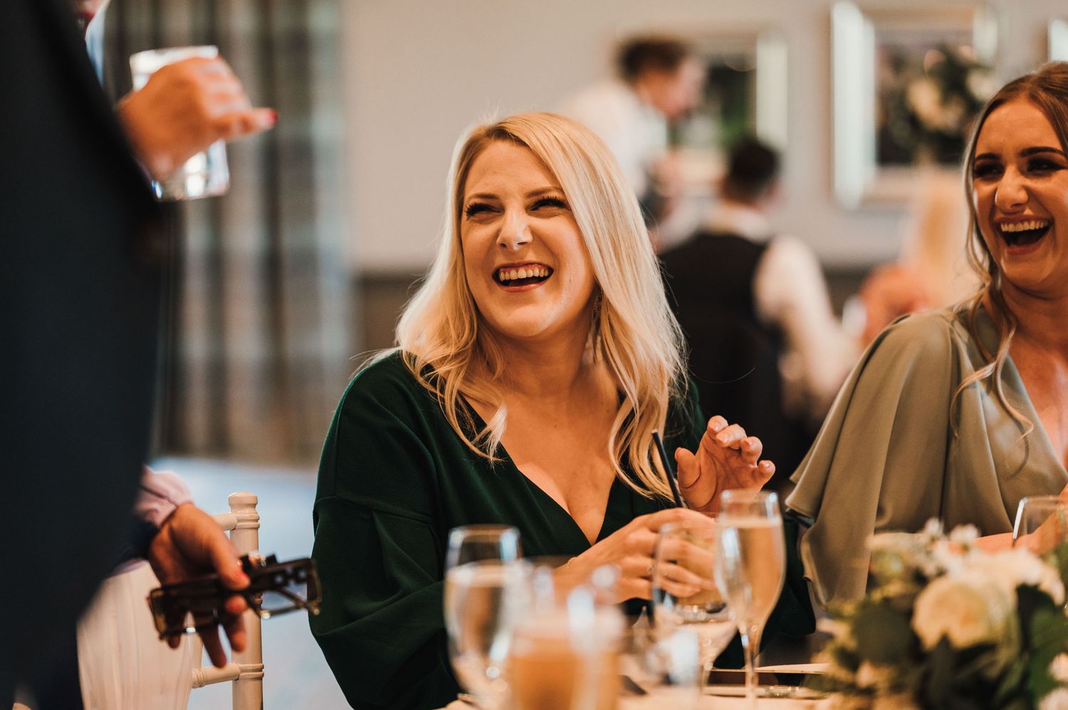 Natural candid moment of guests sharing laughter during wedding reception dinner.