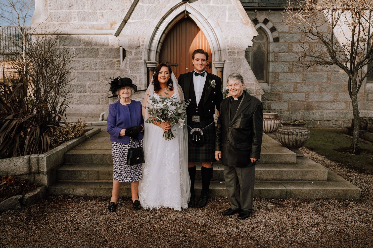 Small family group poses on church steps after wedding ceremony.