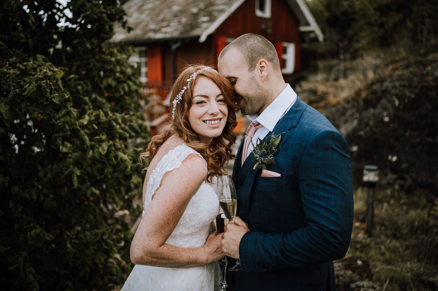 Intimate wedding portrait captured in front of rustic red cabin with natural landscape.