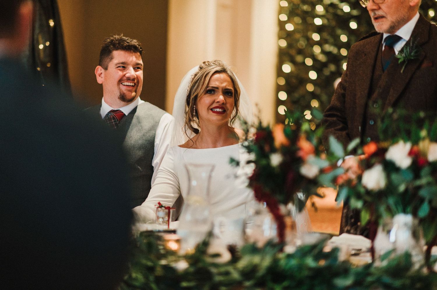A joyful moment captured during wedding speeches with decorative foliage in the foreground.