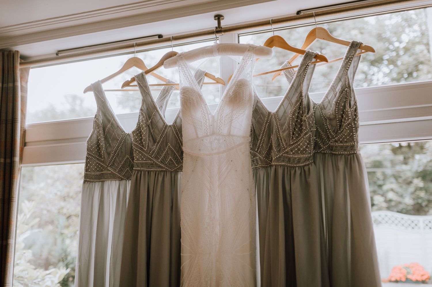 Bridal party dresses in white and sage green displayed against natural window light.
