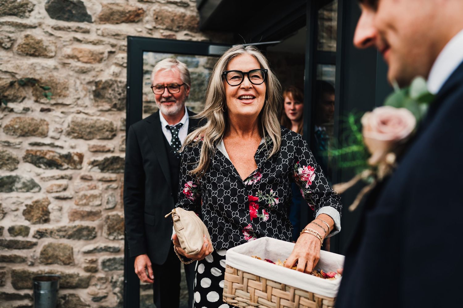 Guest in floral dress laughs while holding basket at outdoor wedding venue.