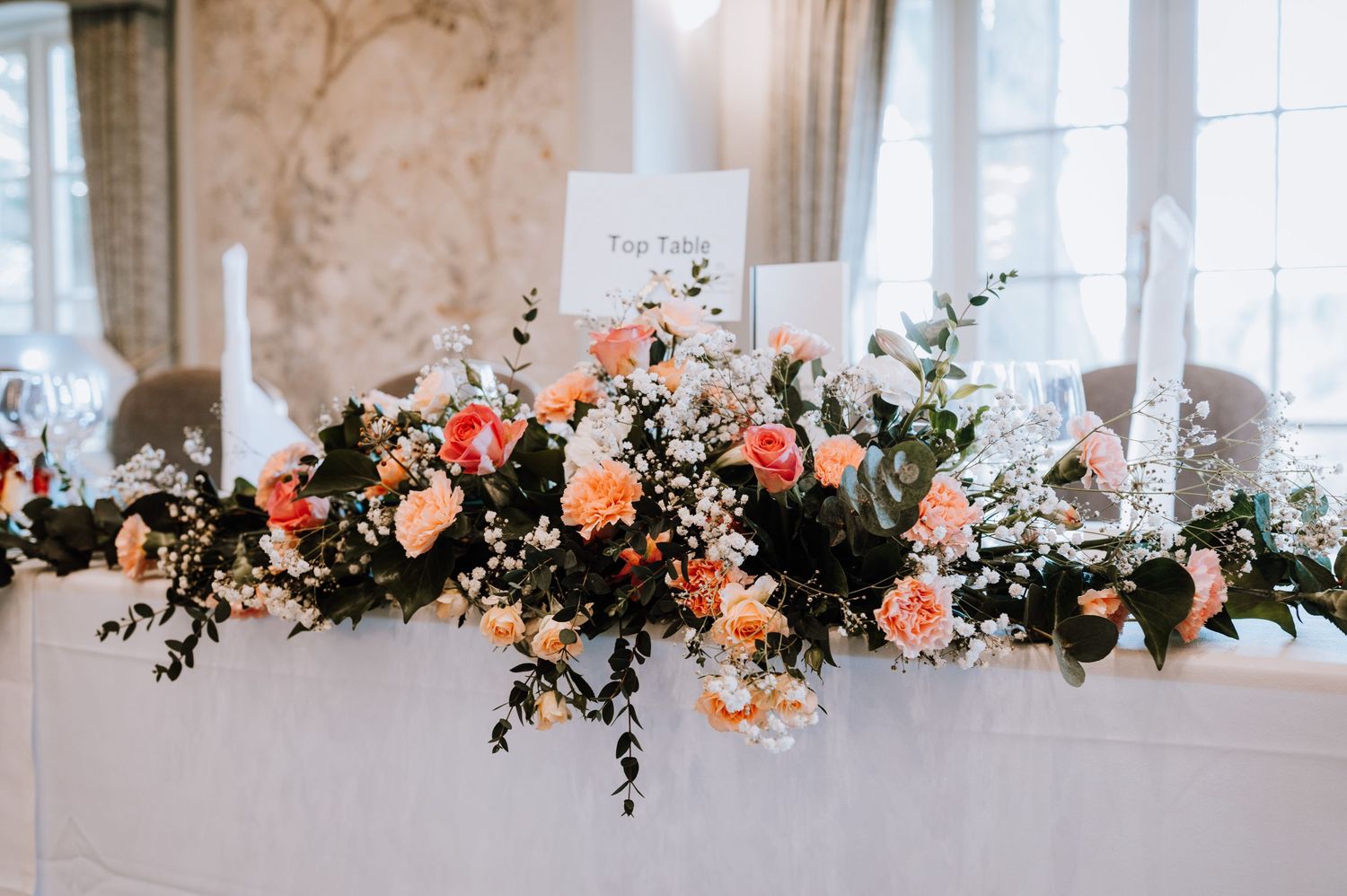 Elegant floral table arrangement with coral and peach blooms mixed with greenery at a wedding reception.