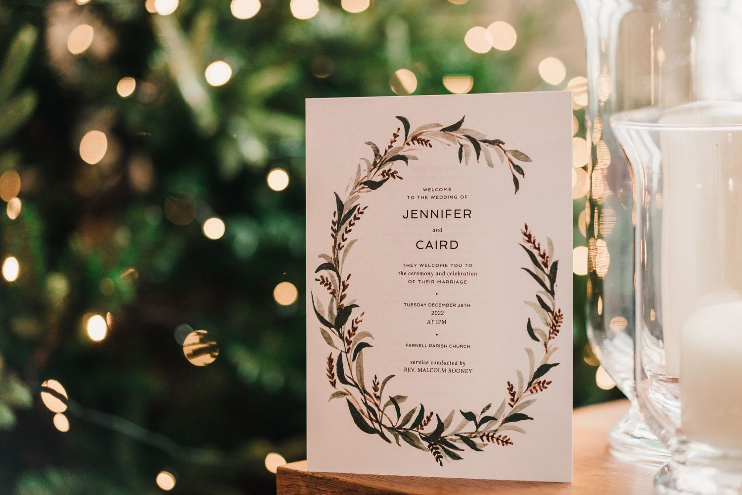 Elegant wedding invitation with floral wreath design displayed against bokeh lights.