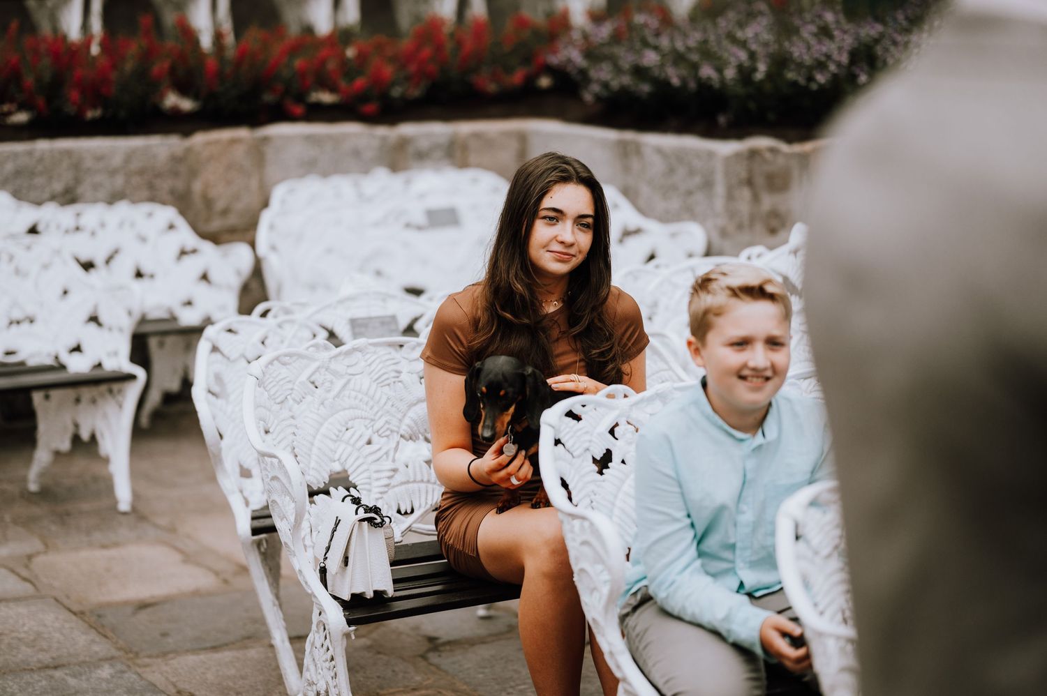 Wedding guests seated on ornate white garden chairs during an outdoor celebration.