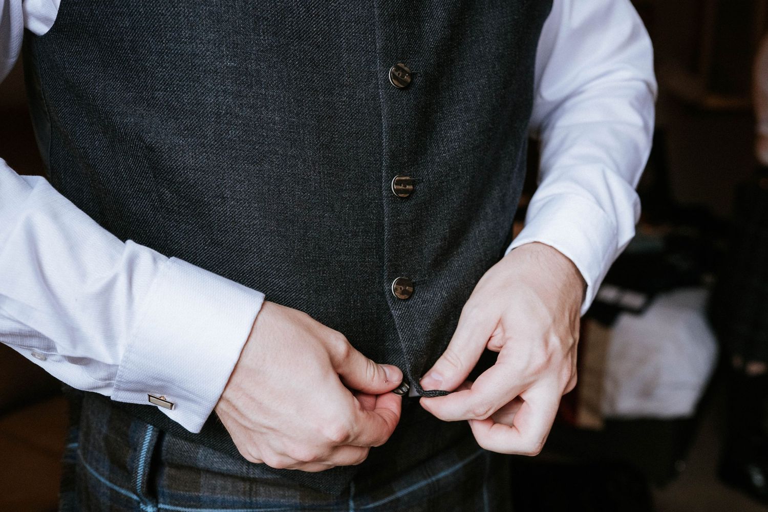Close-up shot of hands buttoning a dark grey vest or waistcoat.