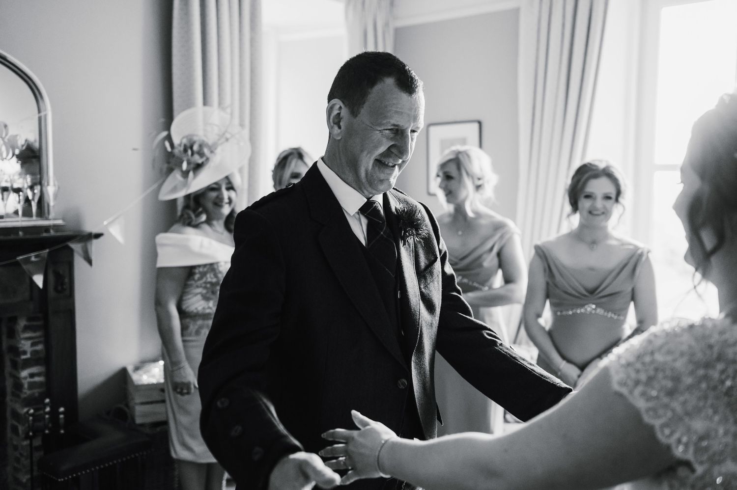 A candid black and white moment captured during wedding preparations in an elegant room with curtained windows.
