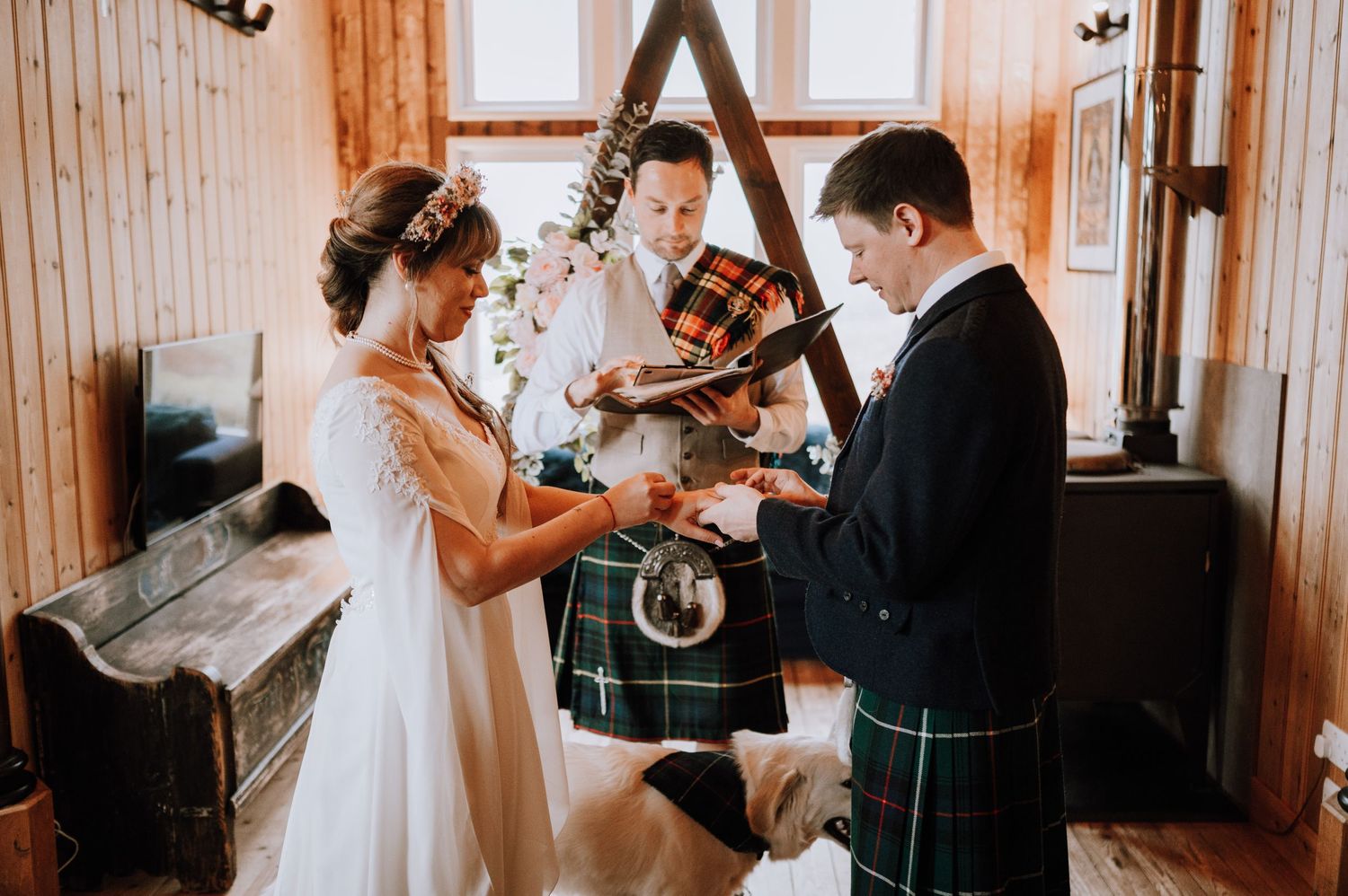 Scottish wedding ceremony in a wooden chapel with traditional kilts and white decor.