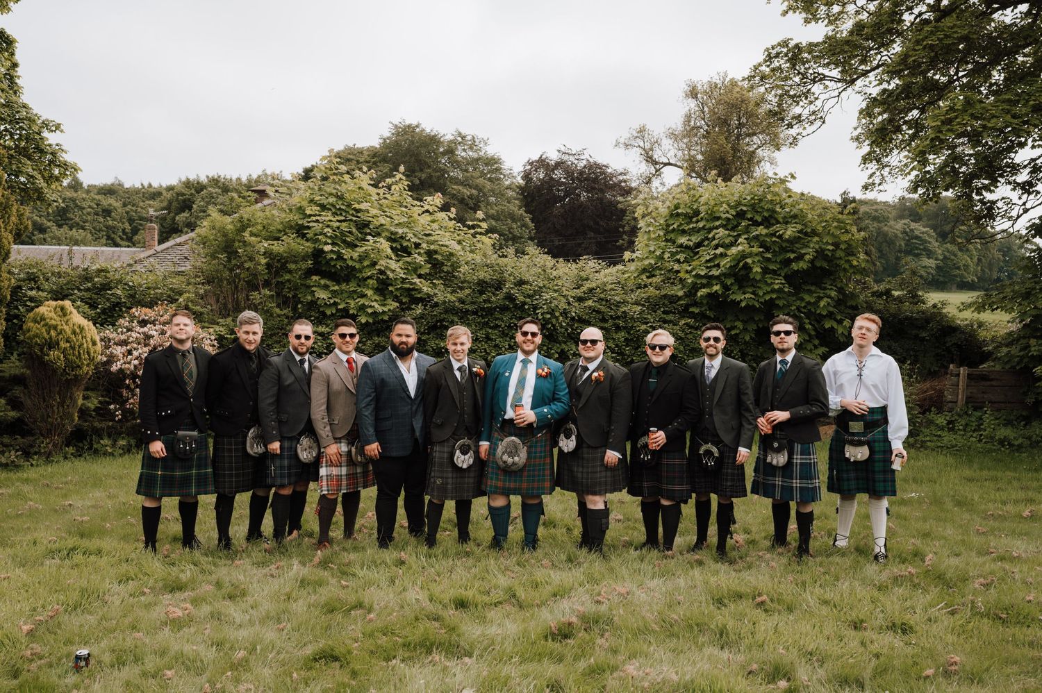 Groomsmen in traditional Scottish kilts stand in line for formal wedding photo.