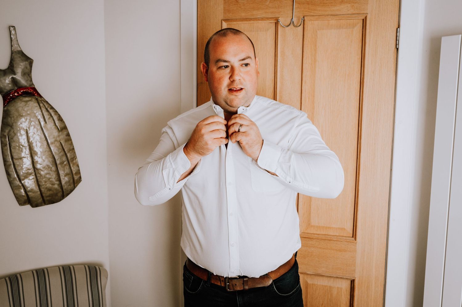 A person adjusting their white shirt collar while standing by a wooden door.