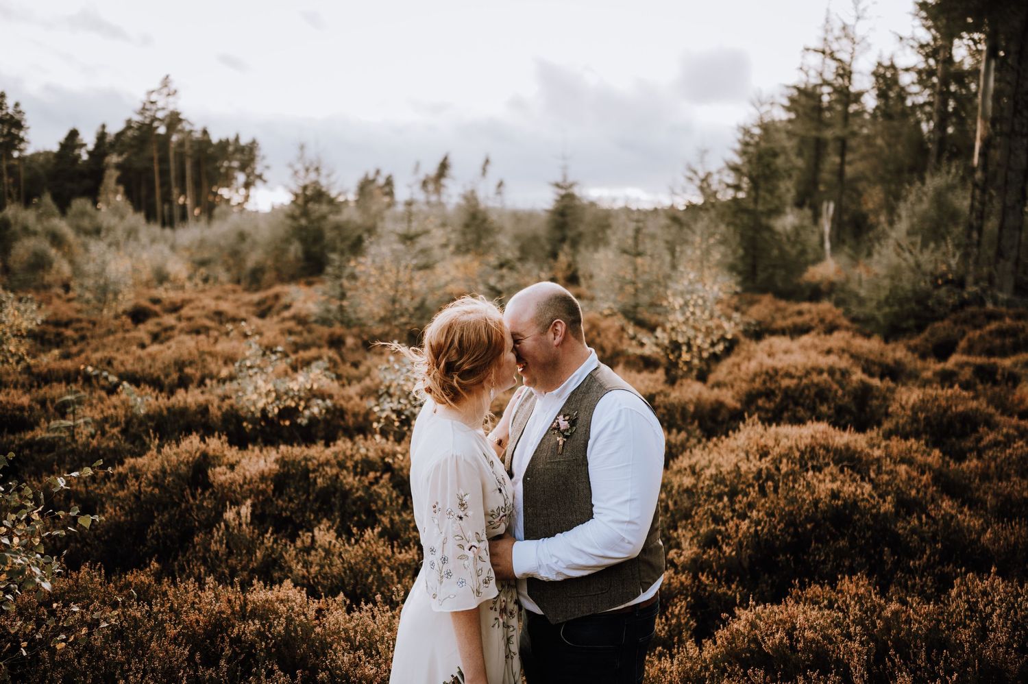 Intimate wedding portrait in a rustic woodland setting with golden ferns and tall trees.
