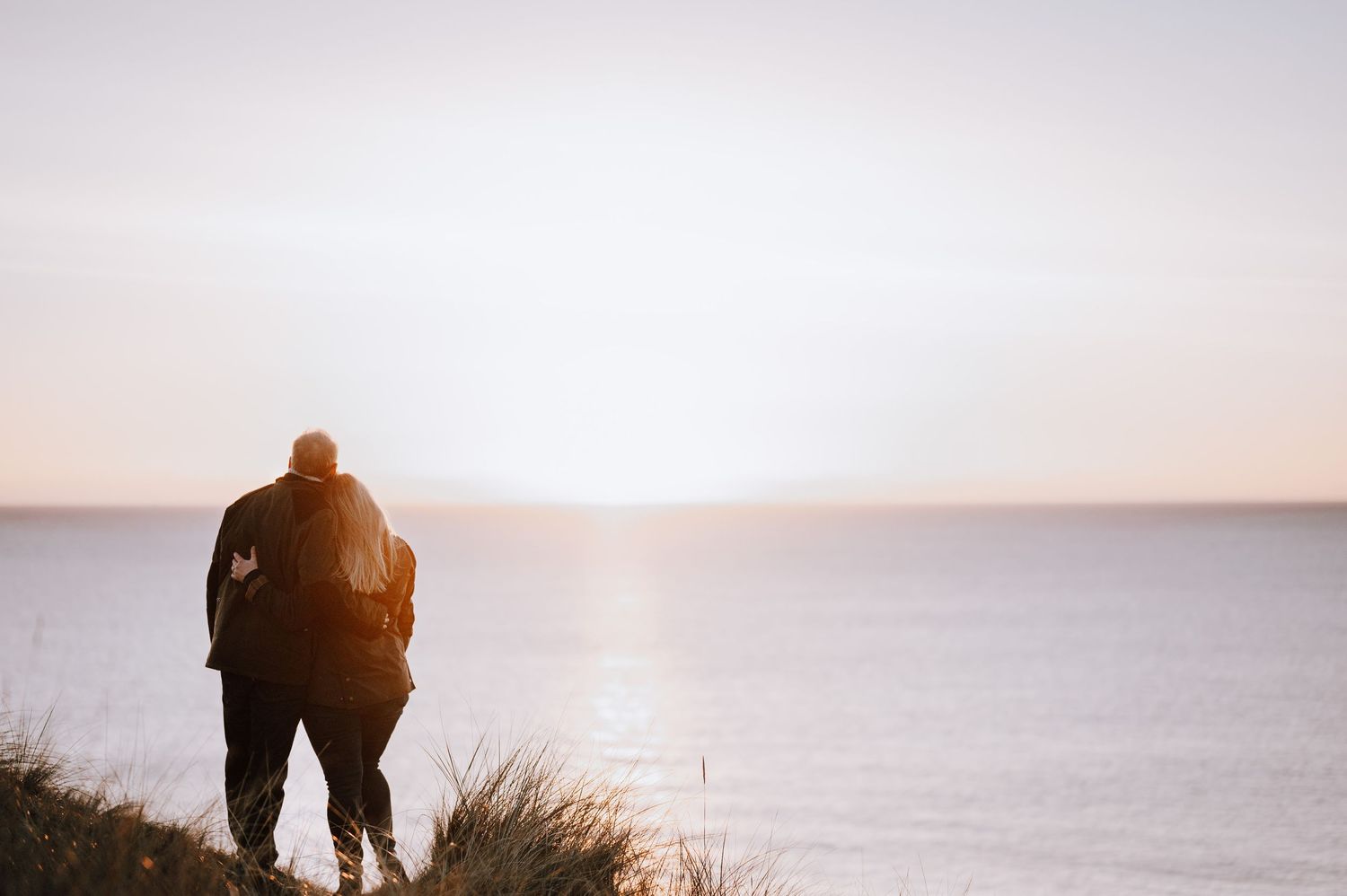A silhouetted figure sits on a cliff edge overlooking a misty ocean during a golden sunset.