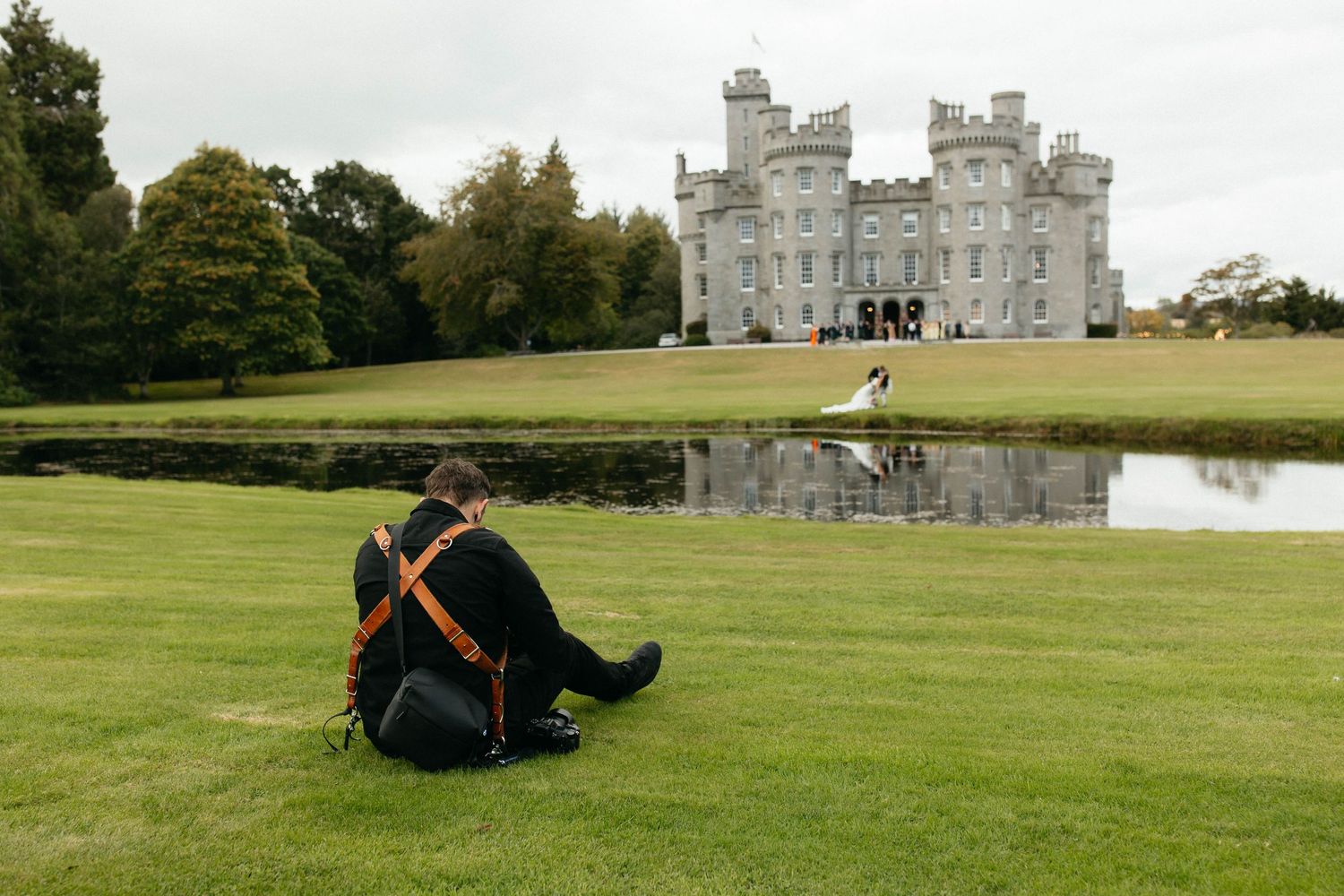 A person lounges on the green lawn in front of a historic stone castle building on a cloudy day.