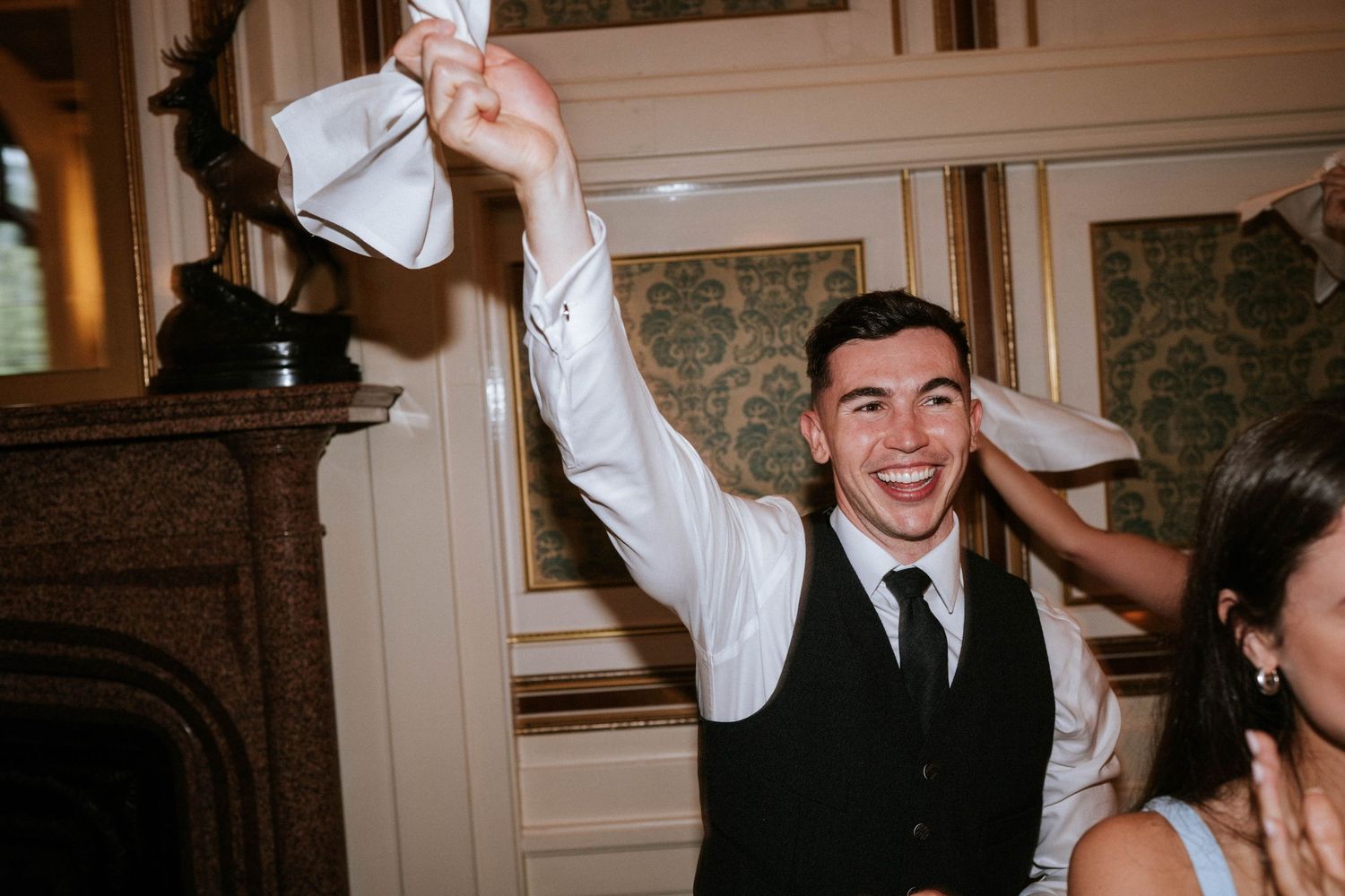 Wedding guests wave napkins in celebration during a festive reception moment.