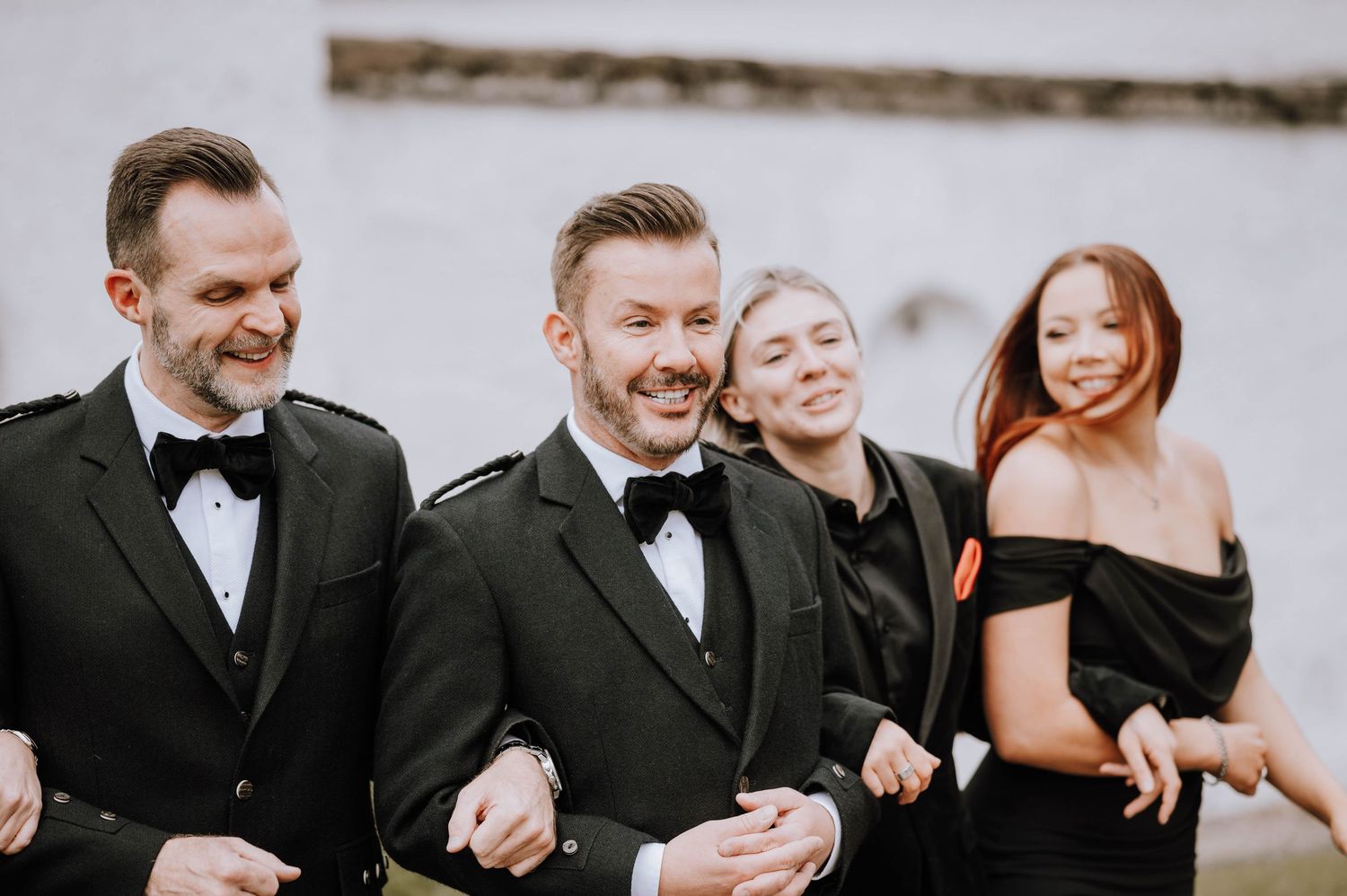 Logie House Wedding Photography. Wedding party sharing joyful moments in formal attire against light colored backdrop.