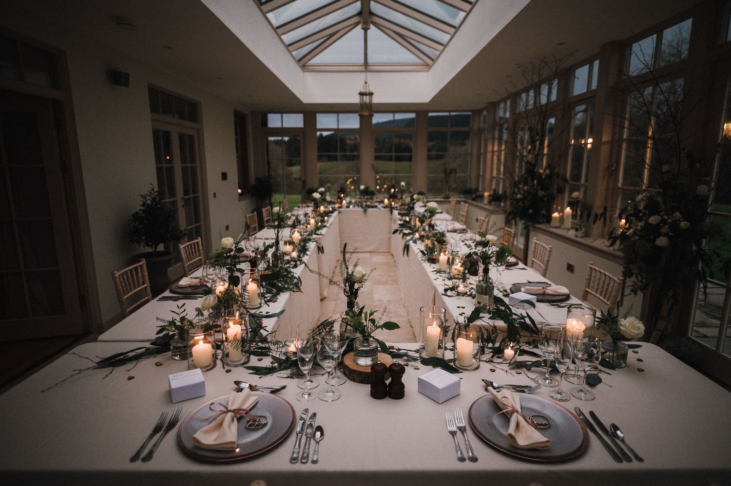 Elegant wedding reception venue with glass ceiling and long tables set for dinner.