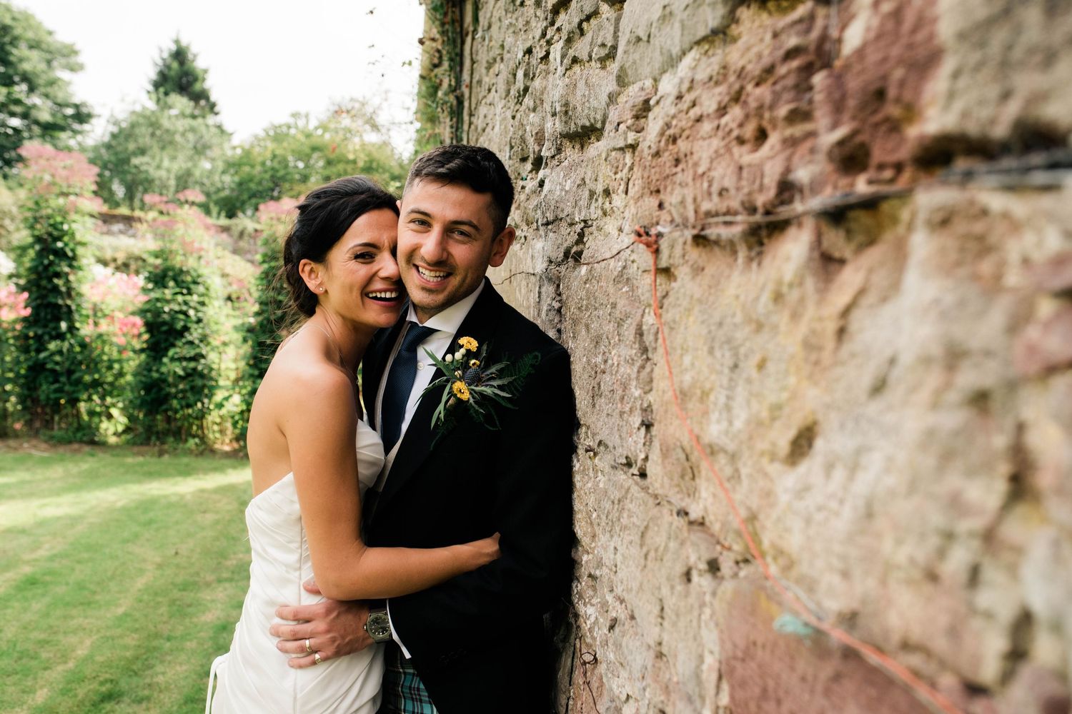 A loving embrace captured against weathered stone walls in a garden setting.