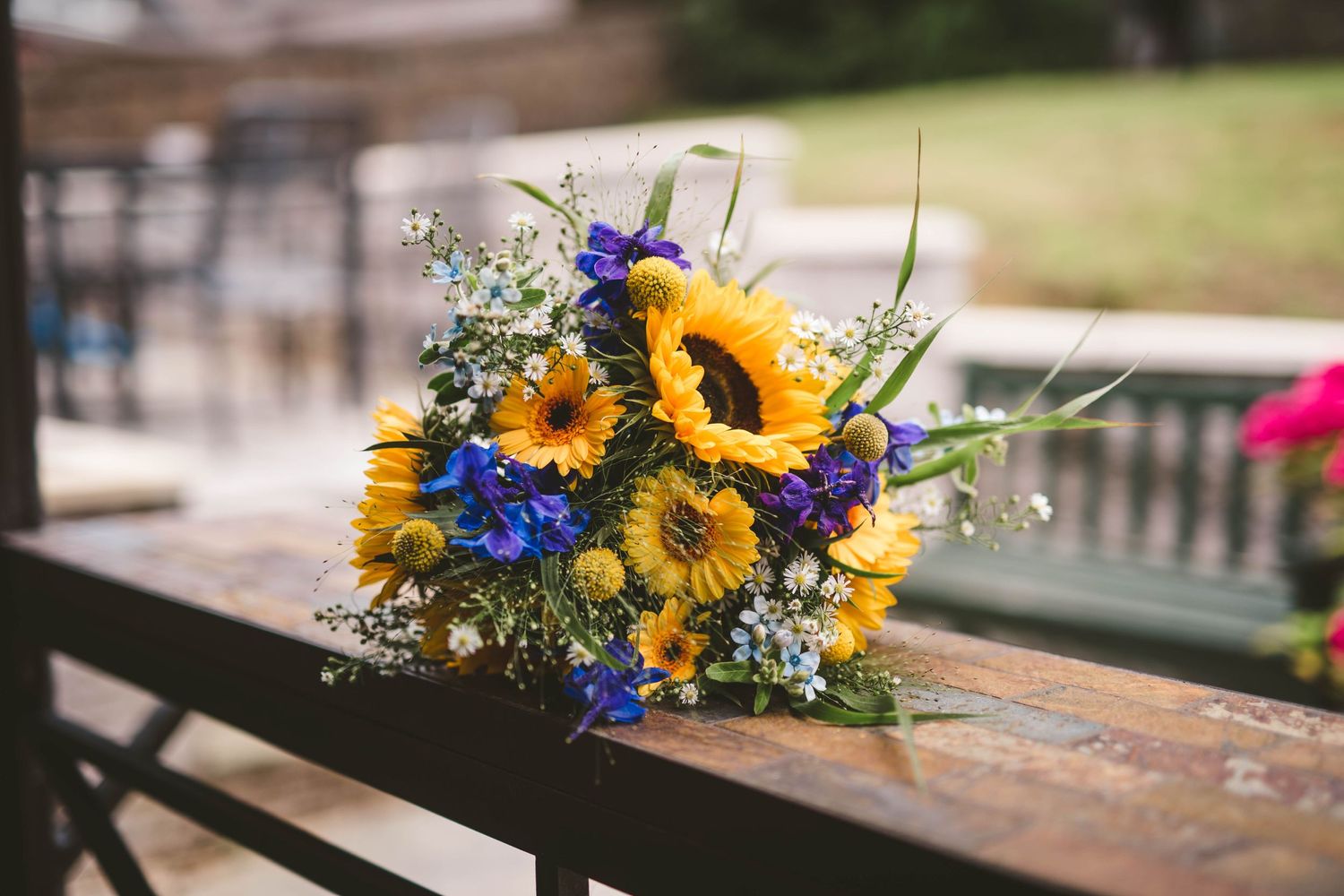 Vibrant sunflower and blue wildflower bouquet arranged on wooden bench outdoors.