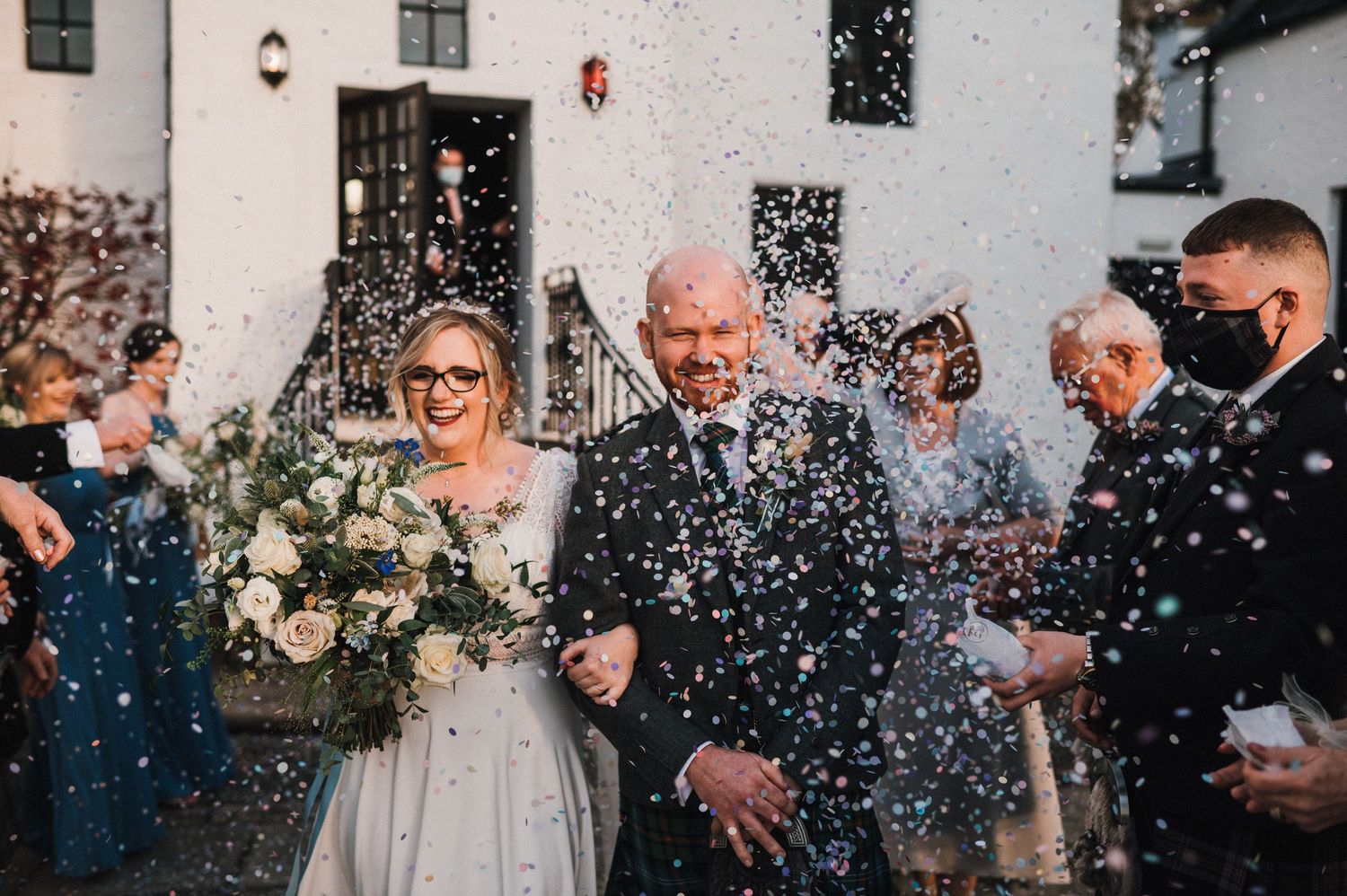 Newlyweds exit their wedding ceremony while guests shower them with confetti in joyful celebration.