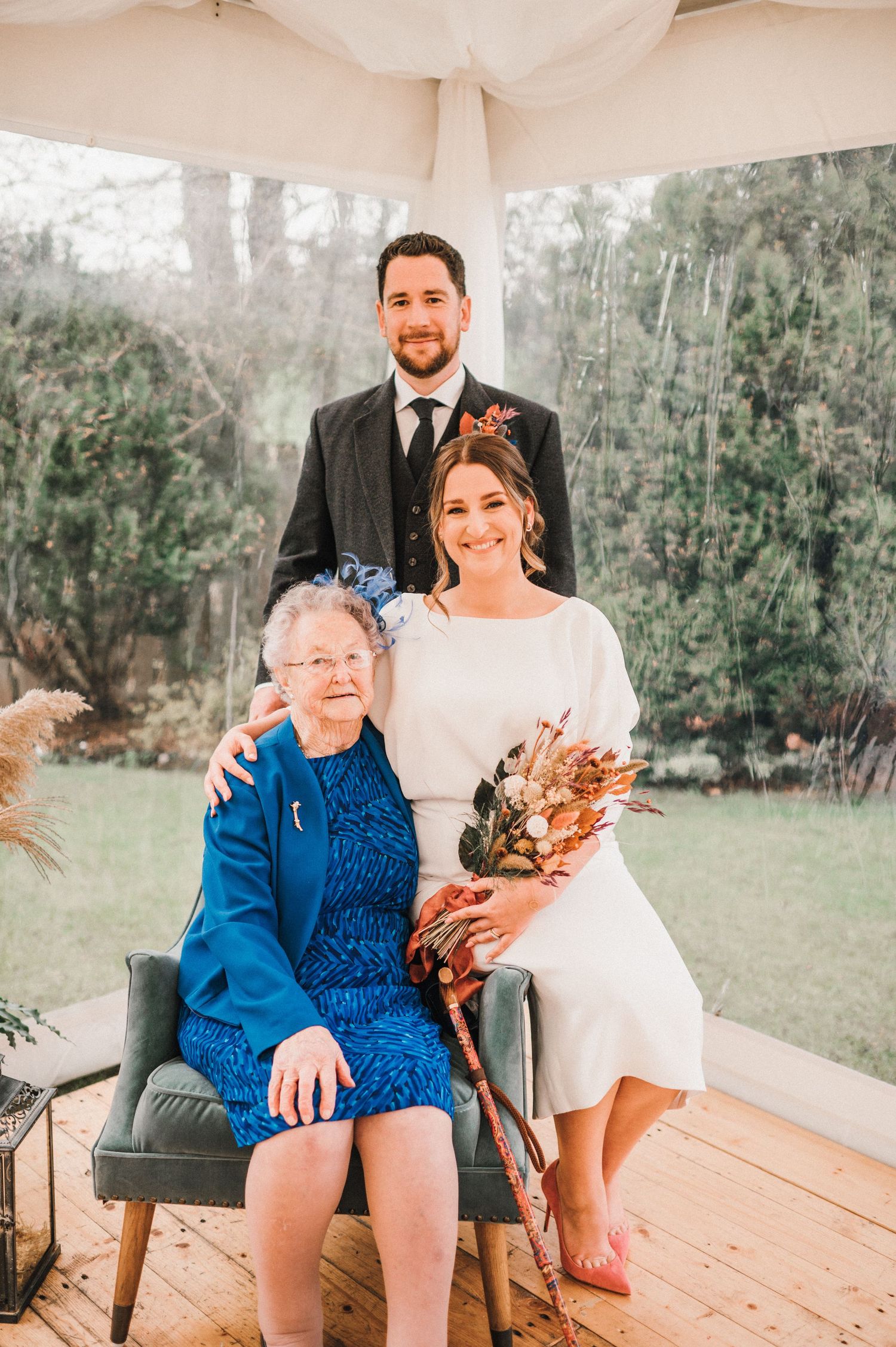 Wedding photo under a white canopy in an outdoor garden setting.