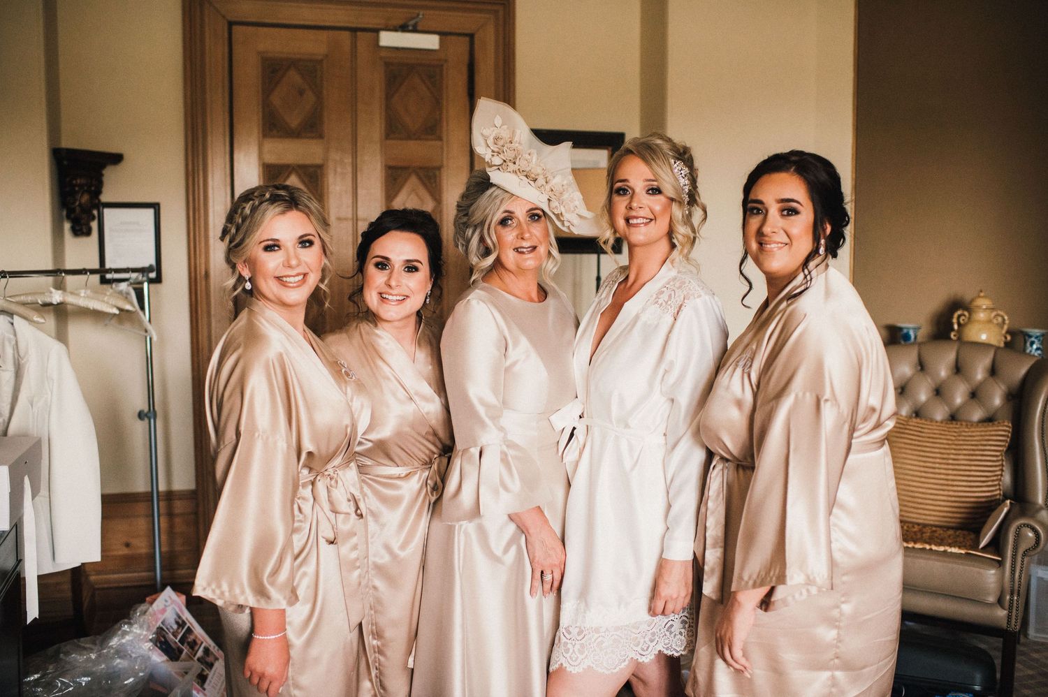 Wedding party in matching blush silk robes pose together in an elegant room with vintage furniture.