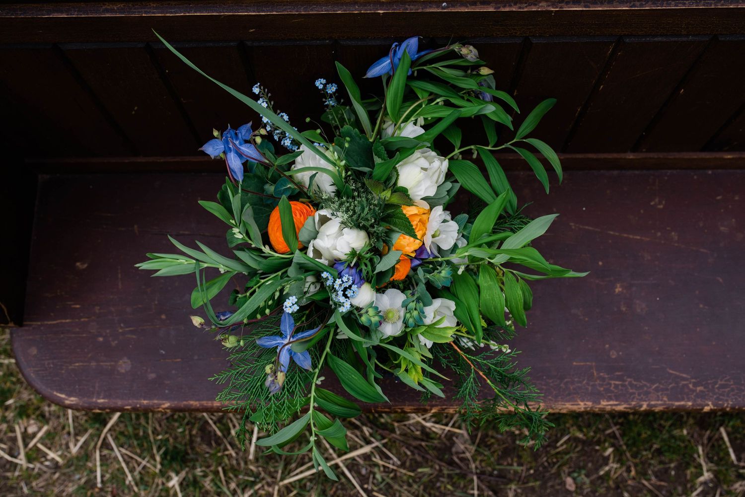 Wedding bouquet with white roses, orange flowers, and blue delphinium resting on wooden steps.