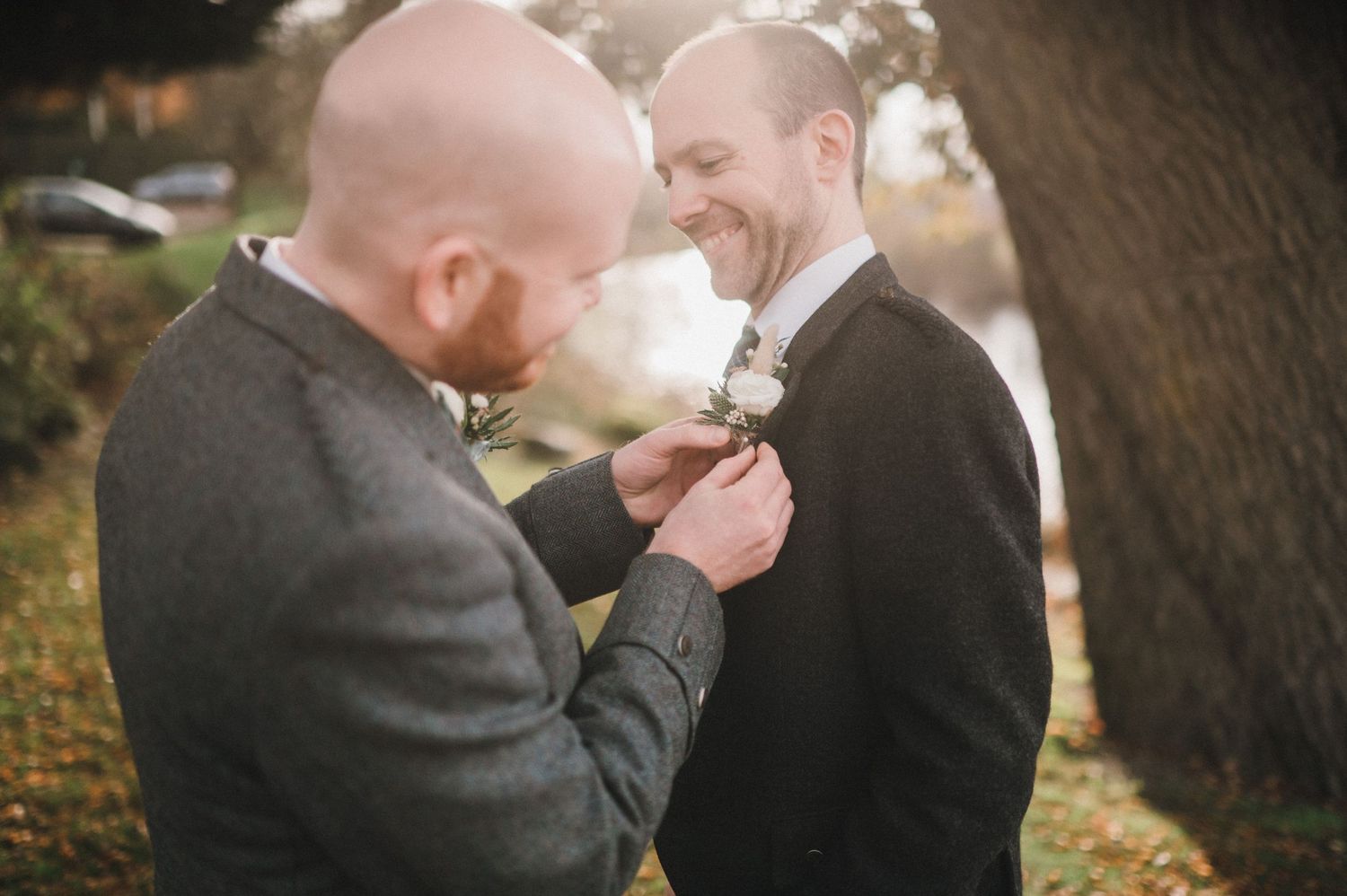 Two people in dark suits sharing an intimate moment outdoors during autumn.