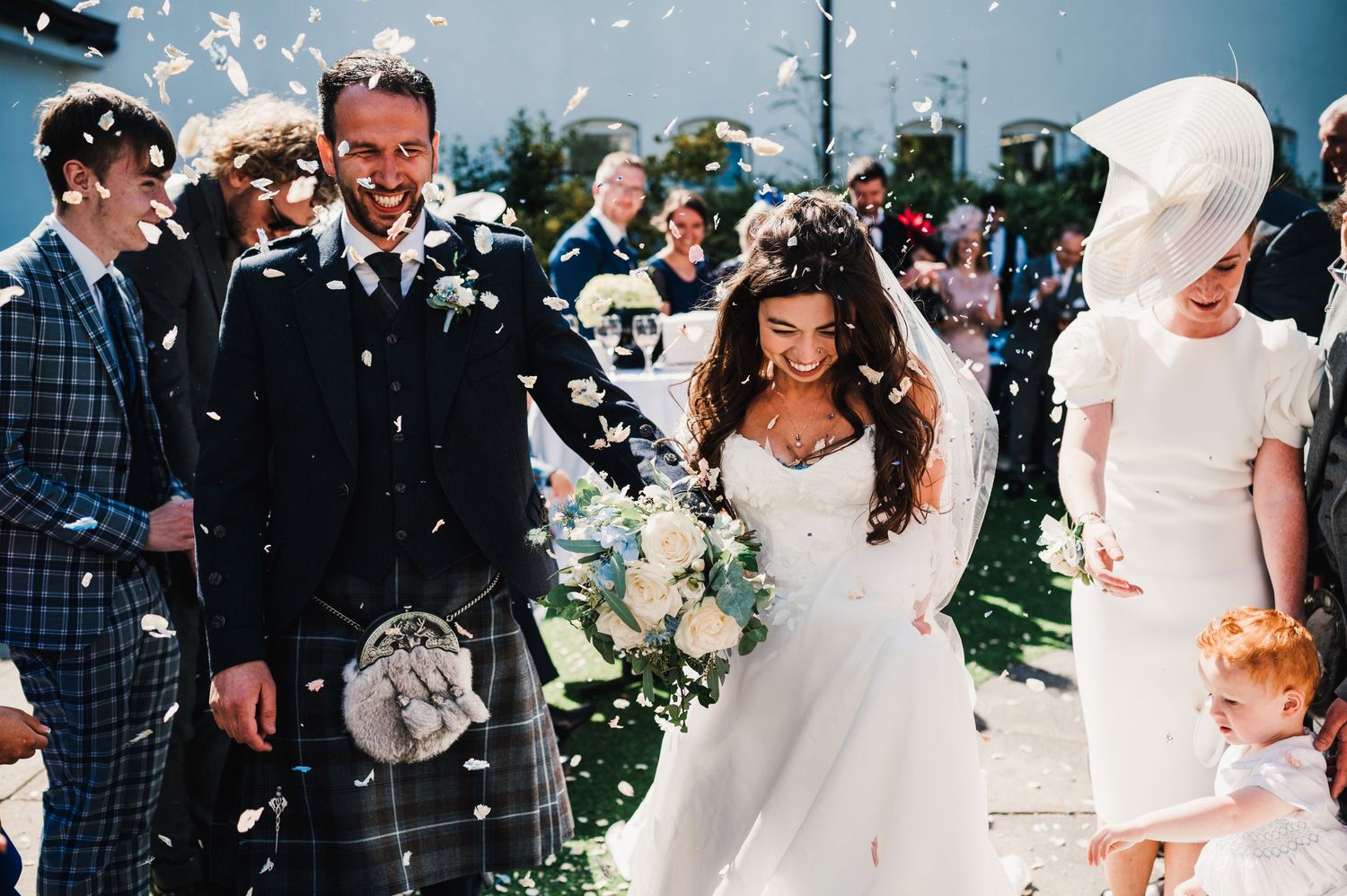 Wedding celebration with traditional Scottish attire amid shower of confetti.