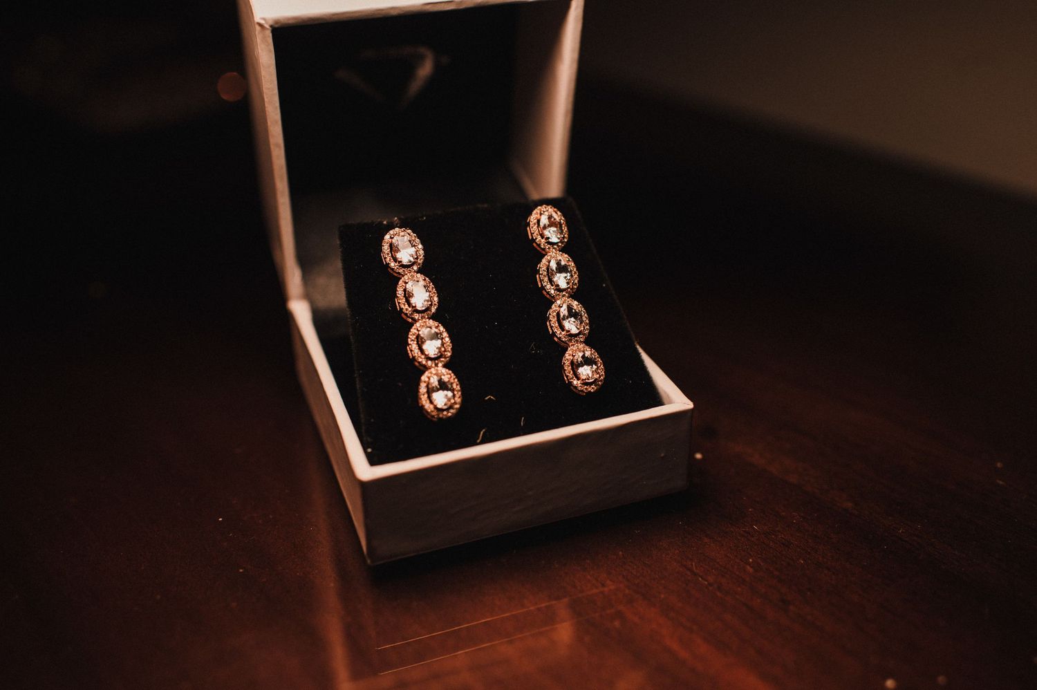 Elegant drop earrings with crystals displayed in a black jewelry box on dark wood surface.