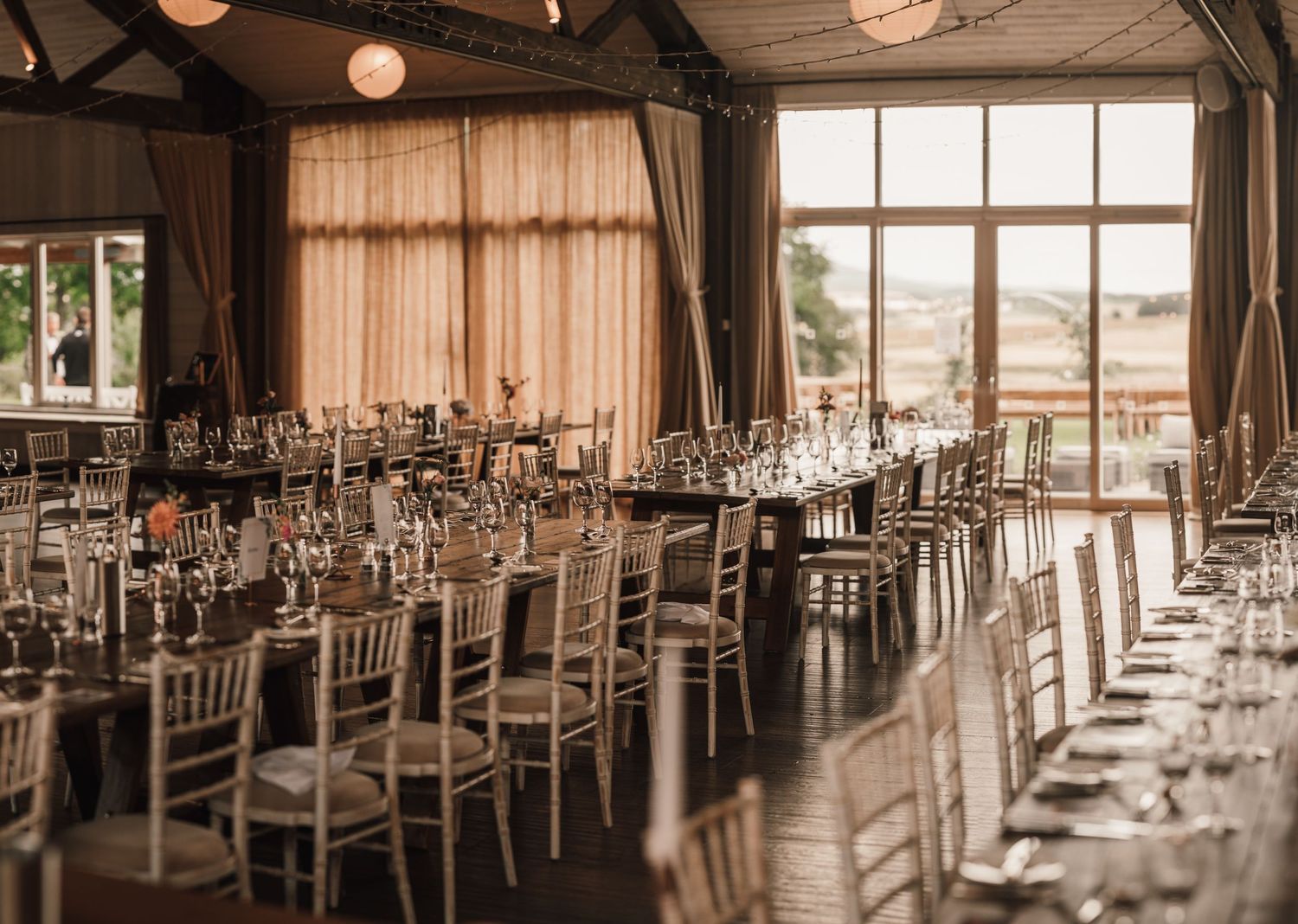 Wedding reception venue with rows of tables set with elegant place settings and chiavari chairs.
