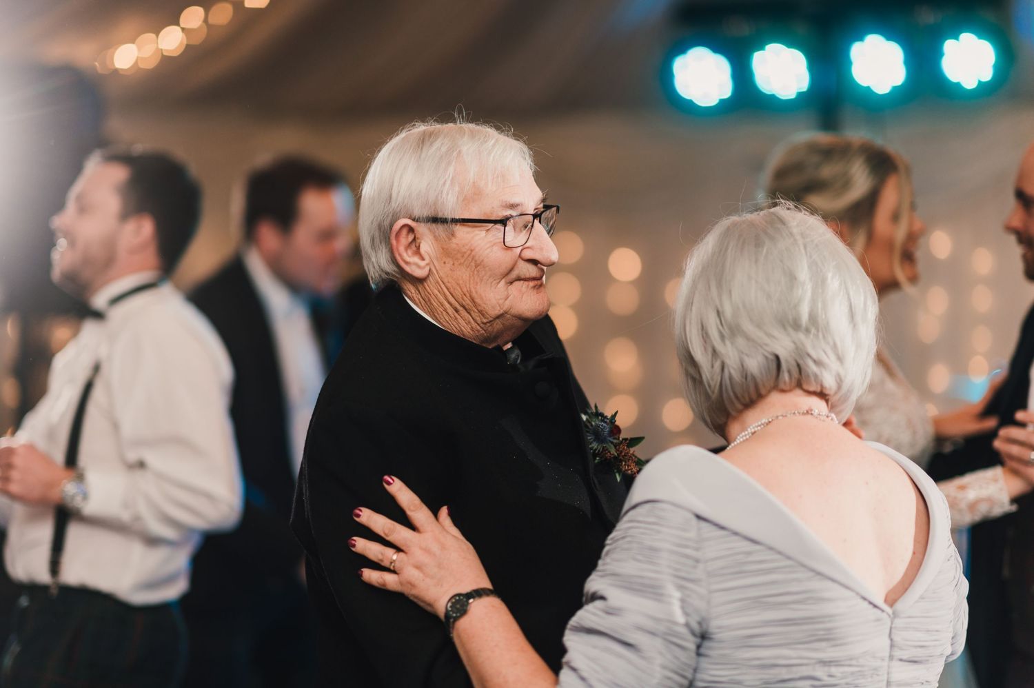 Older couple enjoys dancing together at an elegant wedding reception under ambient lighting.