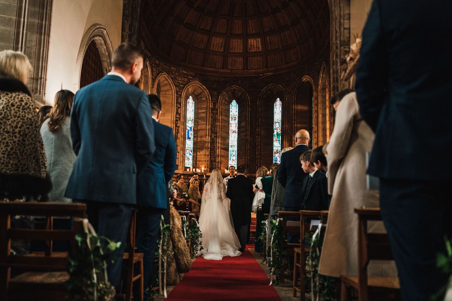 A wide-angle view of a church wedding ceremony with ornate architecture and red carpet aisle.