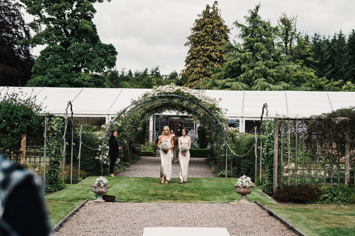 Couple walking through garden archway decorated with flowers at wedding venue.