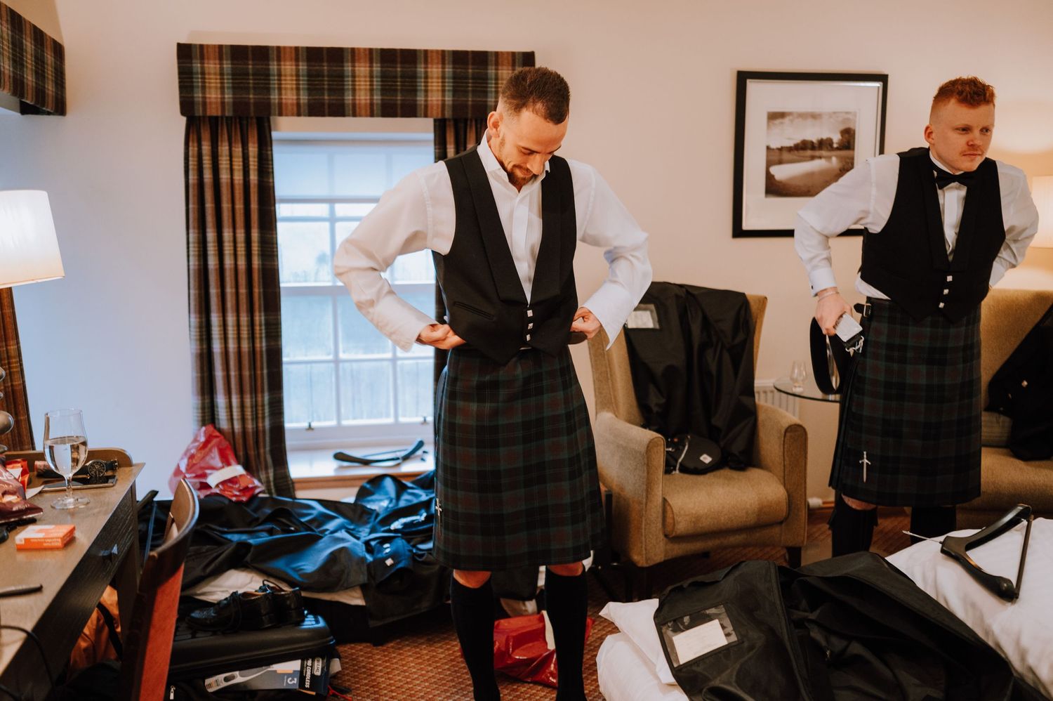 Traditional Scottish kilts and formal wear being fitted in a hotel room.