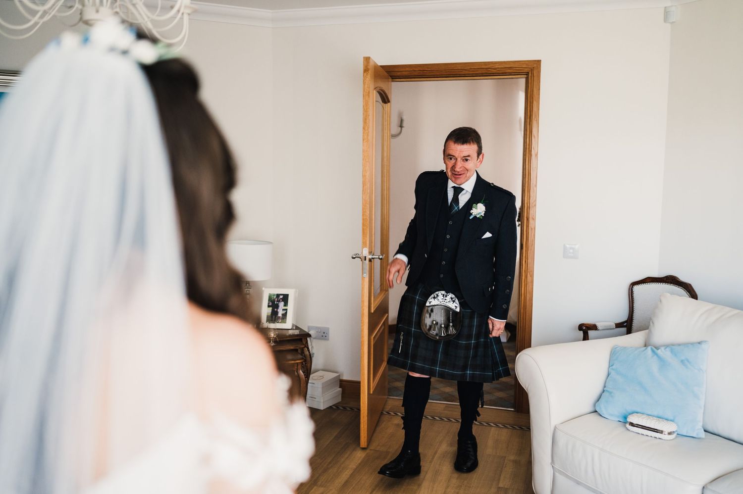 A groom in traditional Scottish kilt attire stands in a doorway before the ceremony.