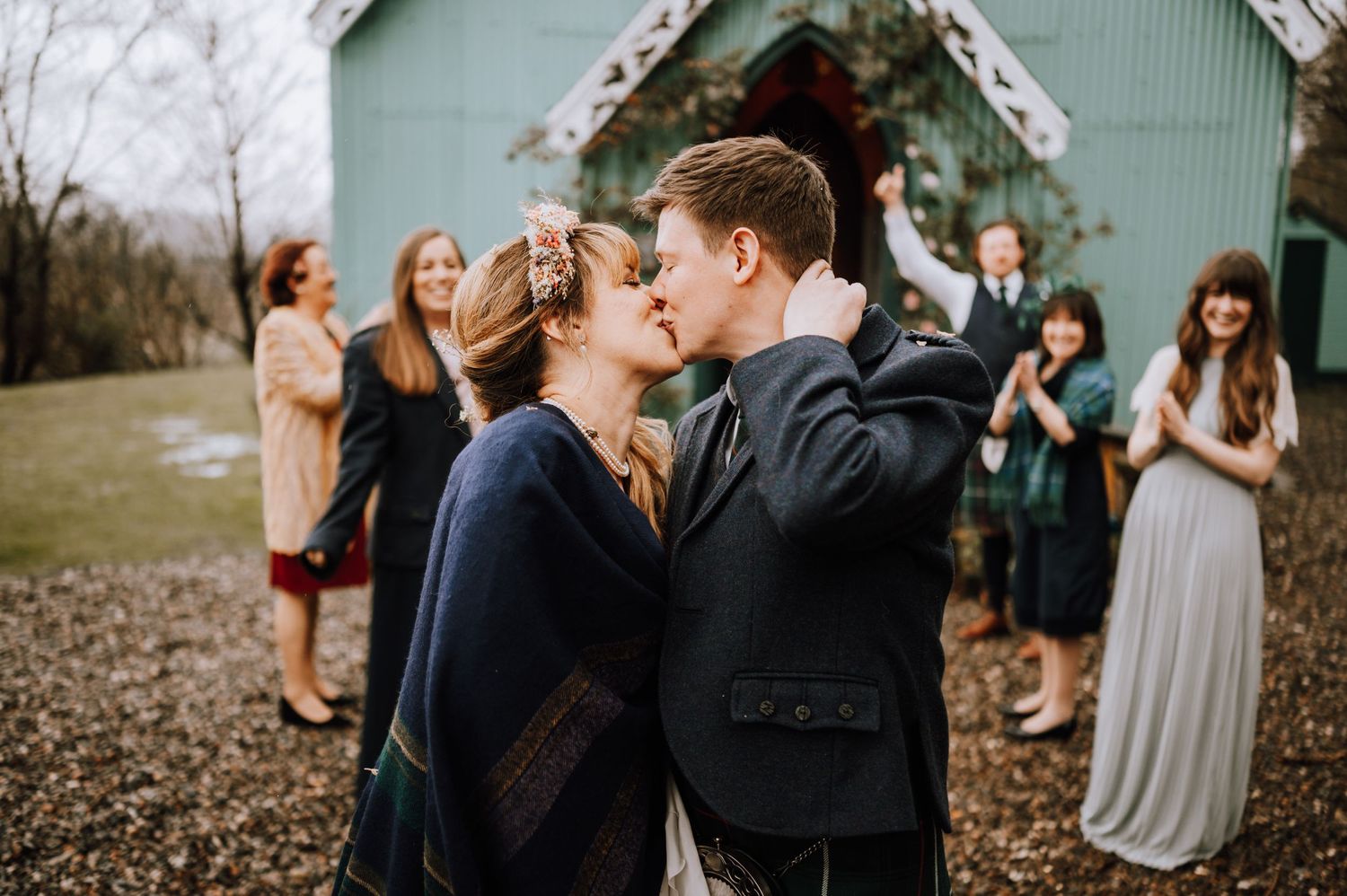 Intimate wedding celebration outside mint green chapel with guests looking on.