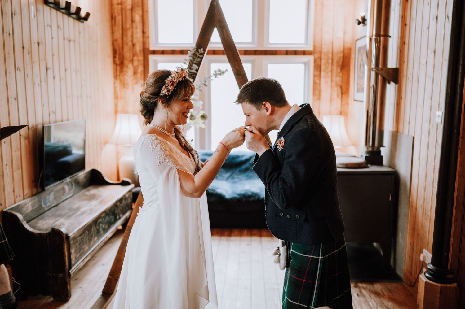A tender moment between a couple in wedding attire near a bright window.