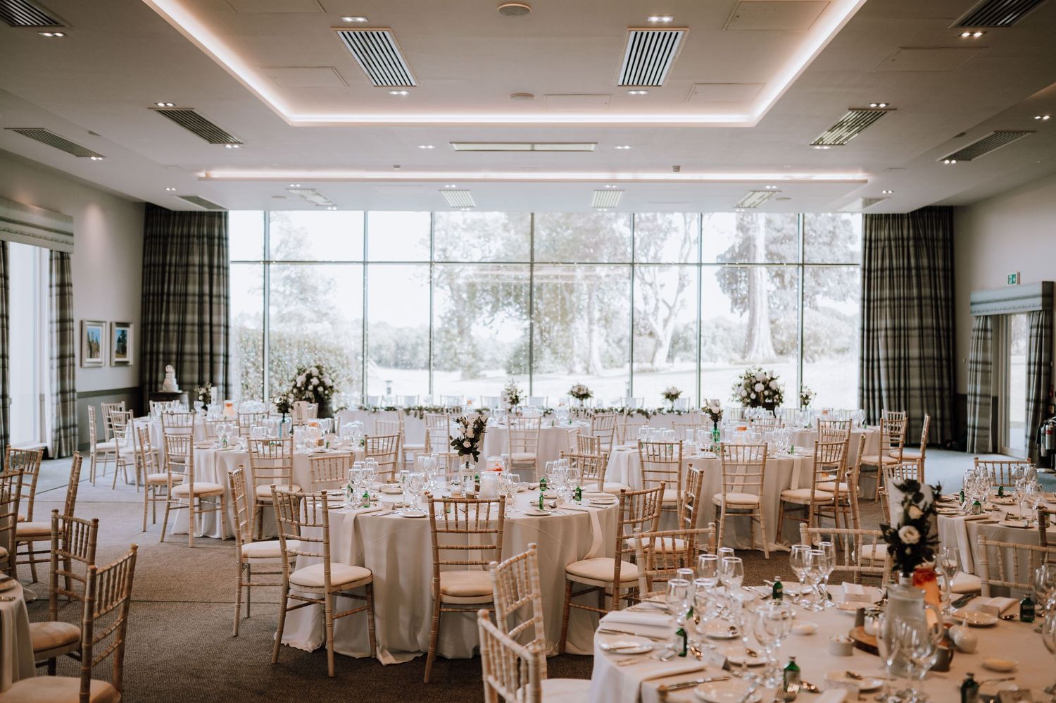 Elegant wedding reception venue with floor-to-ceiling windows, gold chiavari chairs, and white tablecloths.