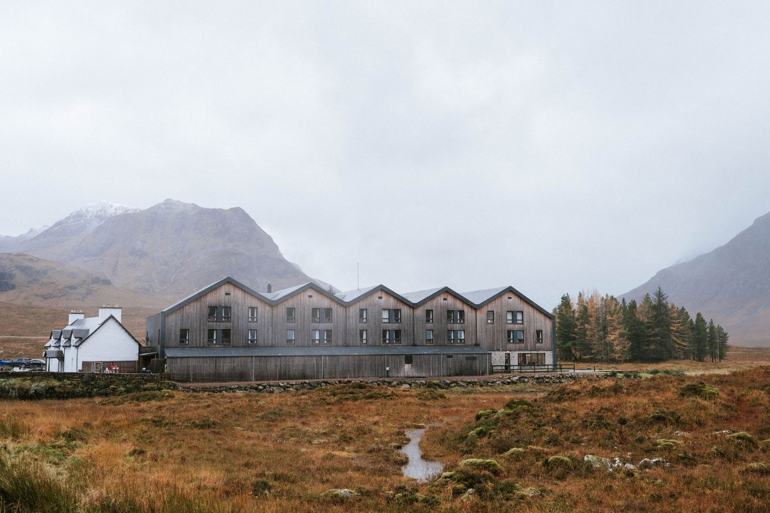 Row of modern lodges nestled in the Scottish Highlands with mountains and autumn colors in background.