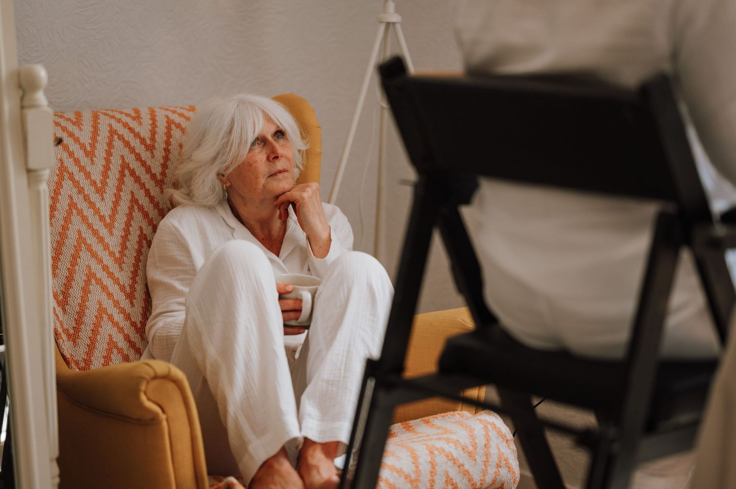 A person relaxes in an orange patterned chair wearing white clothing.