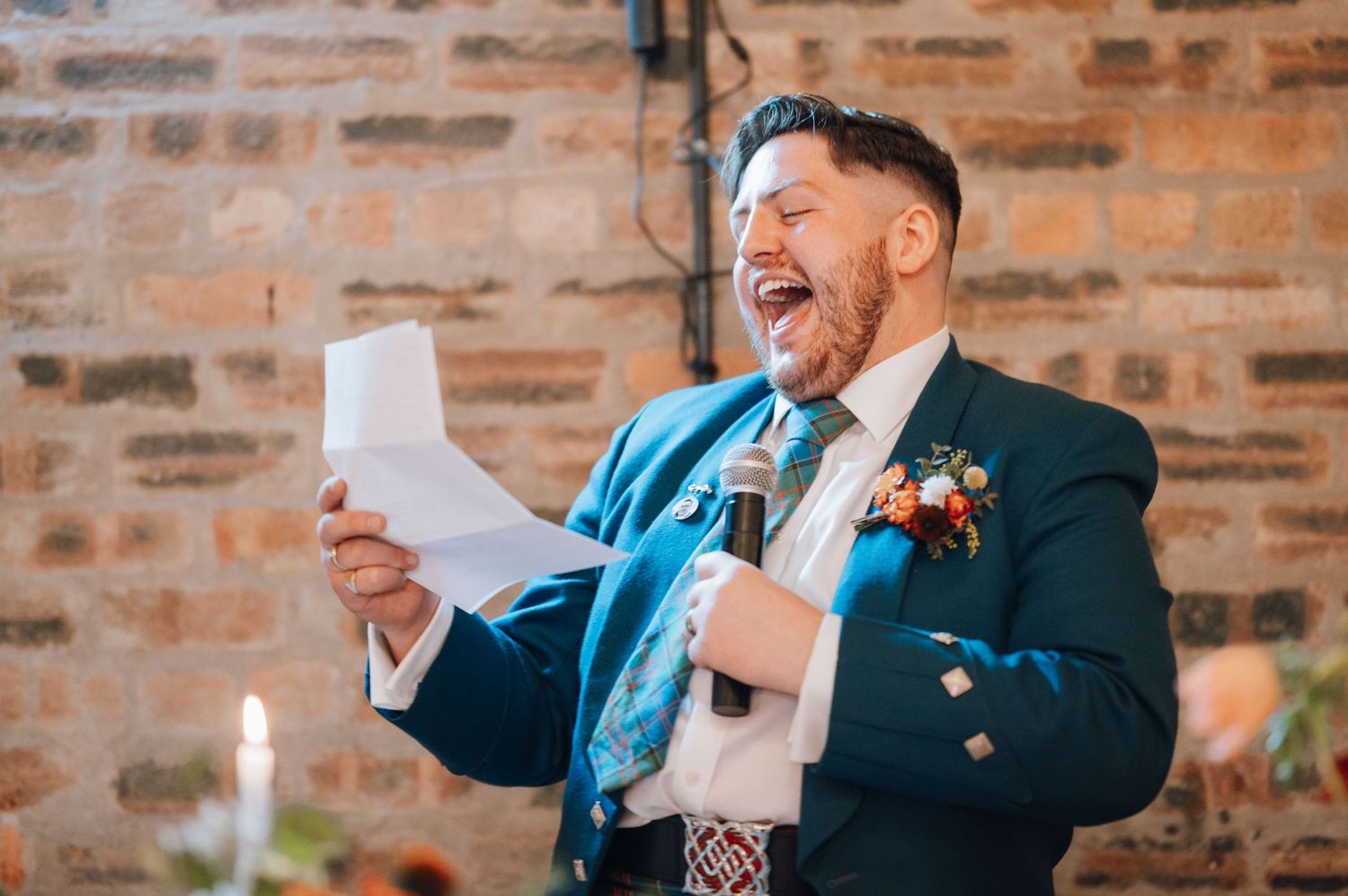 Wedding guest gives emotional speech at reception with brick wall backdrop.
