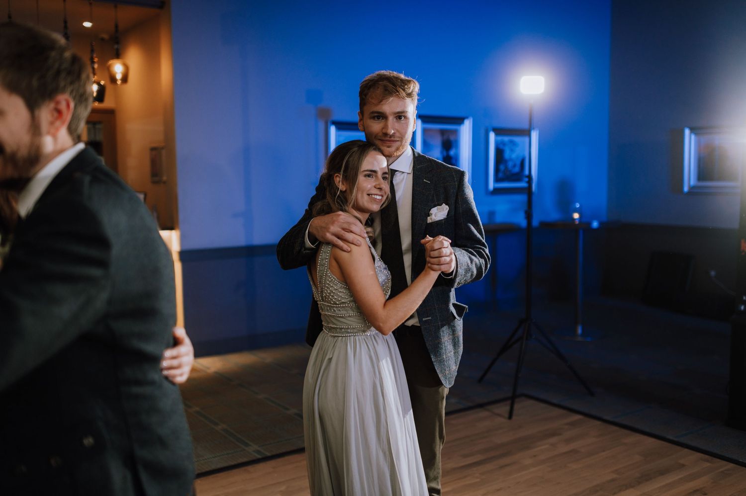Couples embrace while slow dancing at an evening wedding reception with blue lighting.