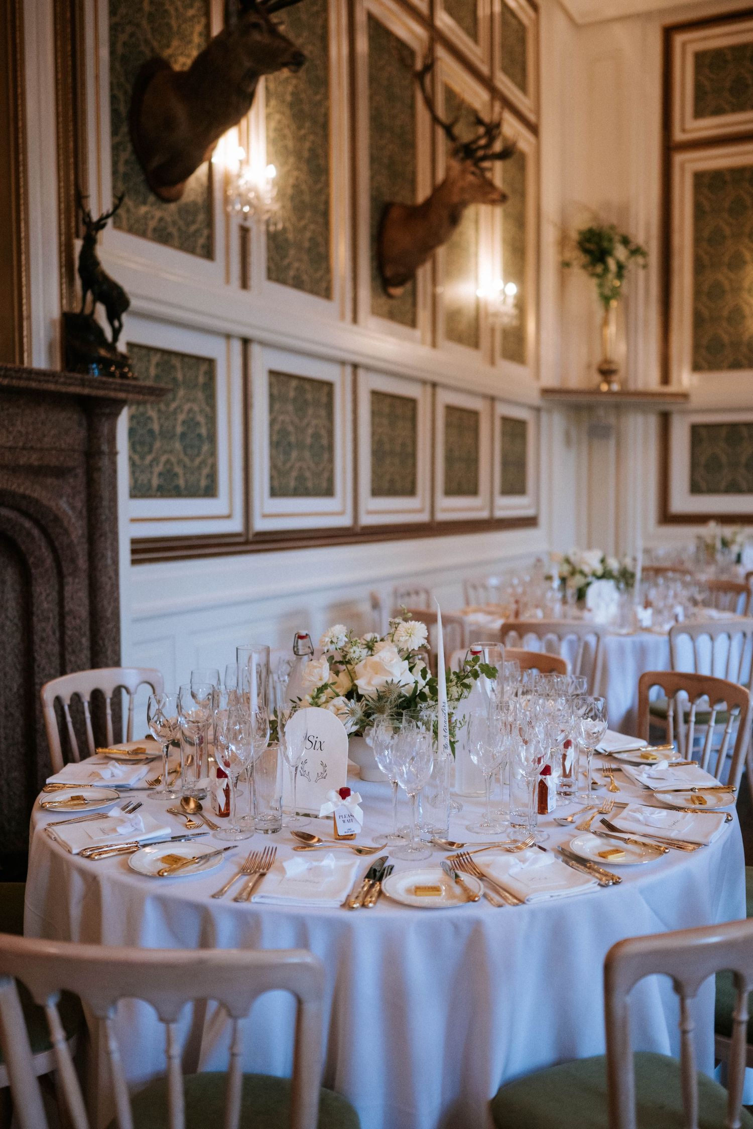 Wedding reception tables set with formal place settings and white linens in grand dining room.