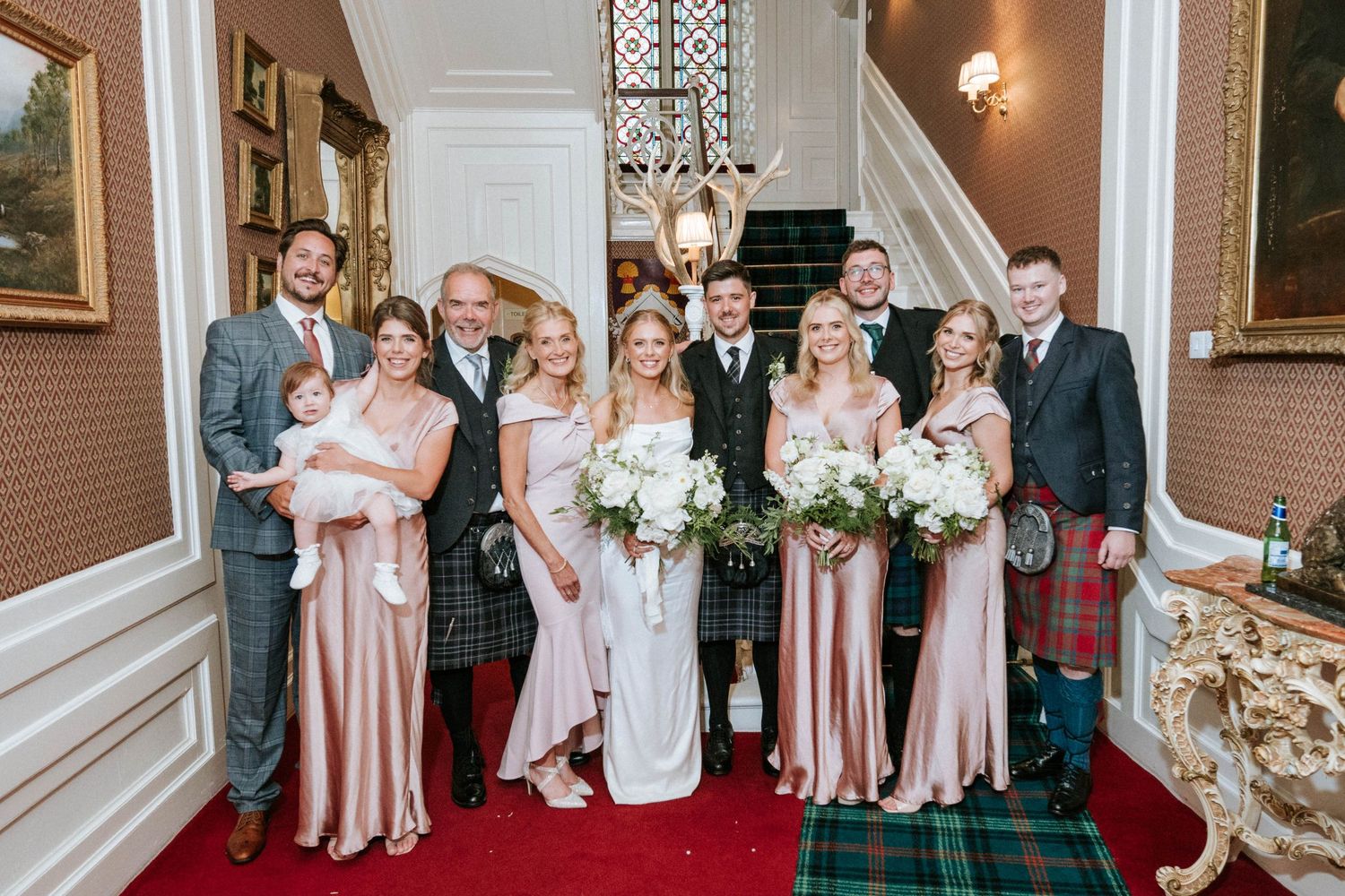Wedding party lined up in formal attire against classic interior with white molding.