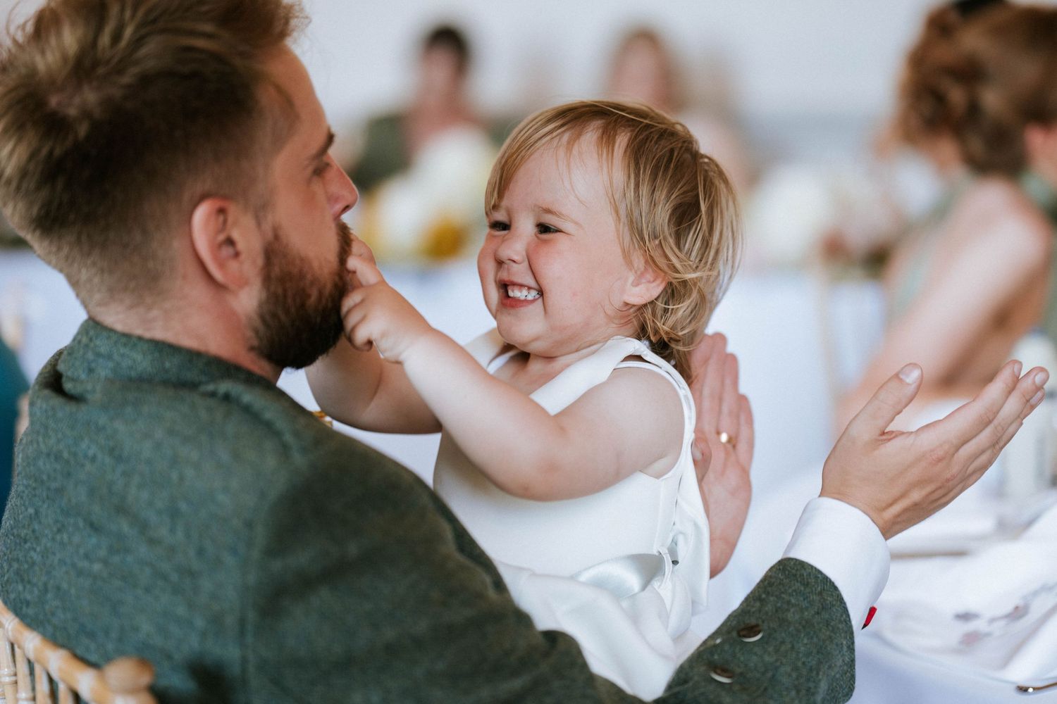Heartwarming moment between parent and laughing toddler during wedding reception.