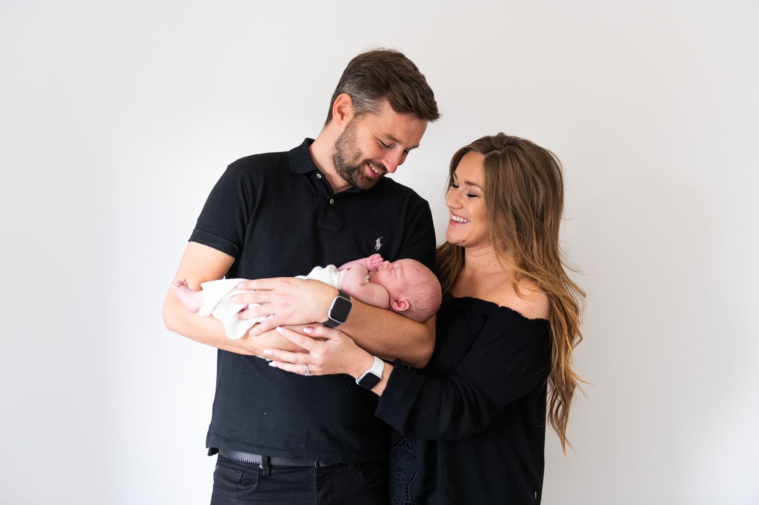 Parents sharing a tender moment with their newborn baby against a white studio backdrop.