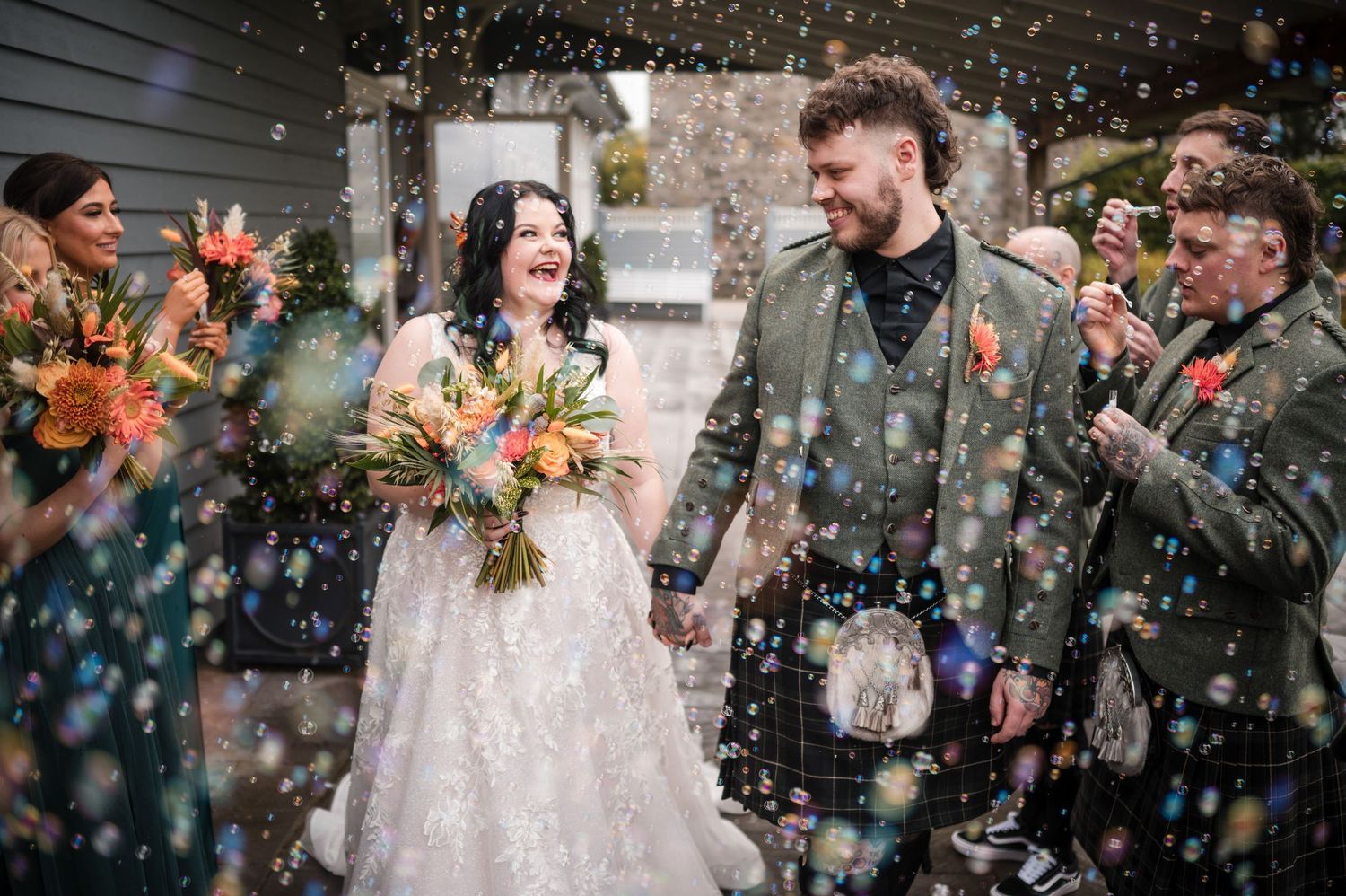 Newlyweds walk through falling confetti as wedding guests celebrate during an outdoor ceremony.