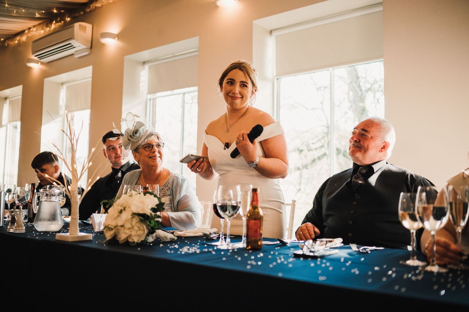 Logie House Wedding Photography. Wedding celebration guests raising glasses and cheering at decorated reception table.